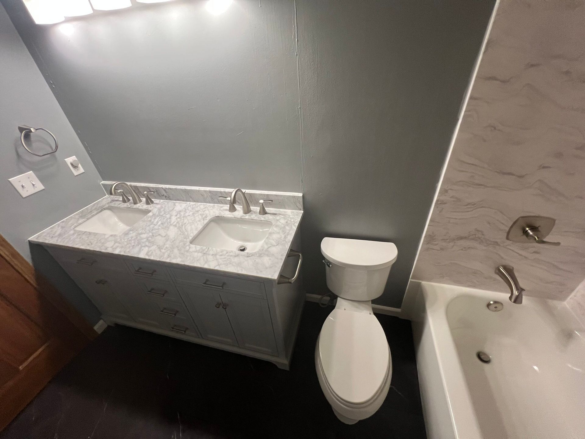 Modern gray bathroom with sink vanity, toilet, and bathtub under bright vanity lights