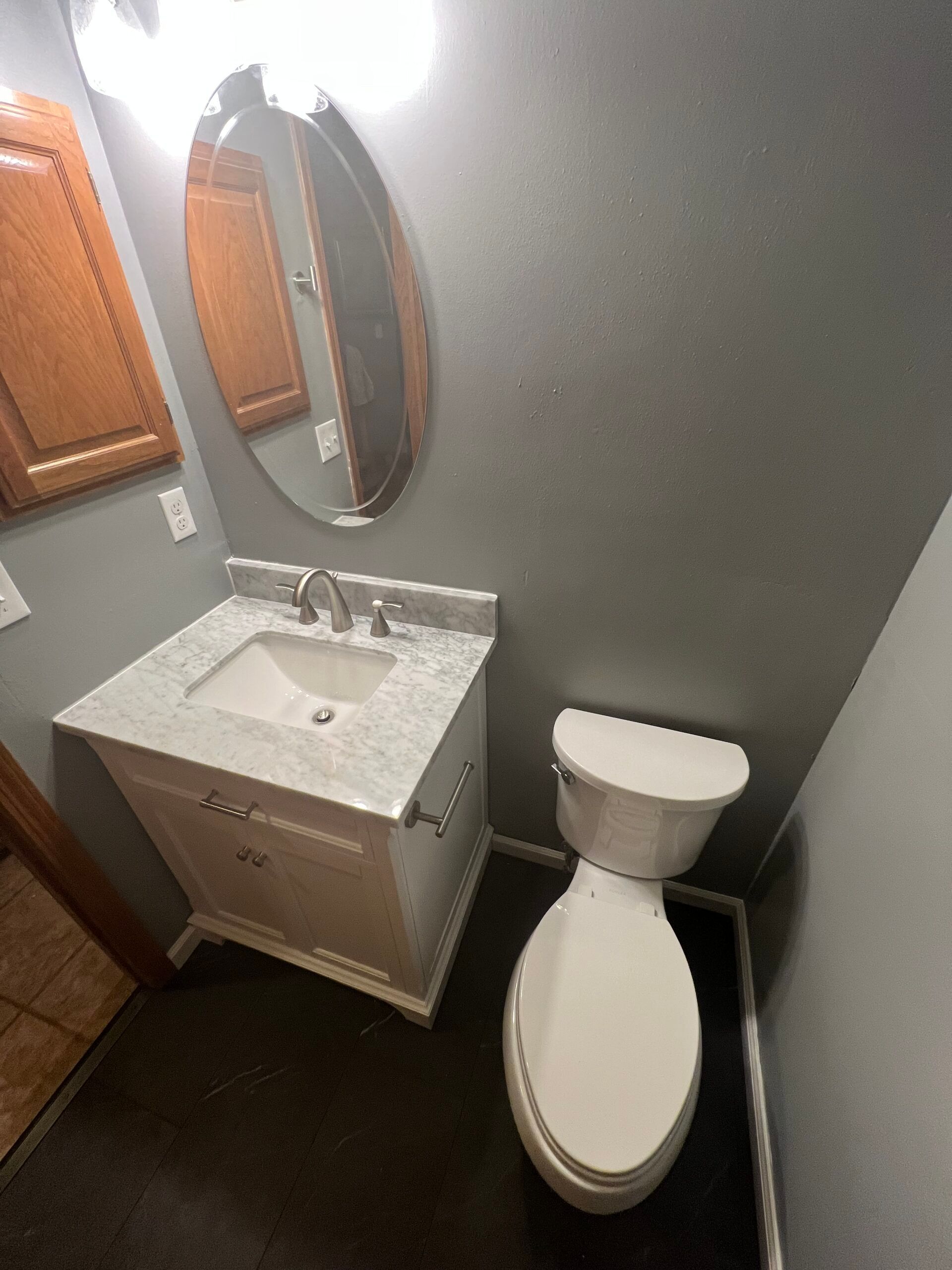 Small bathroom with a sink, oval mirror, and toilet against gray walls.