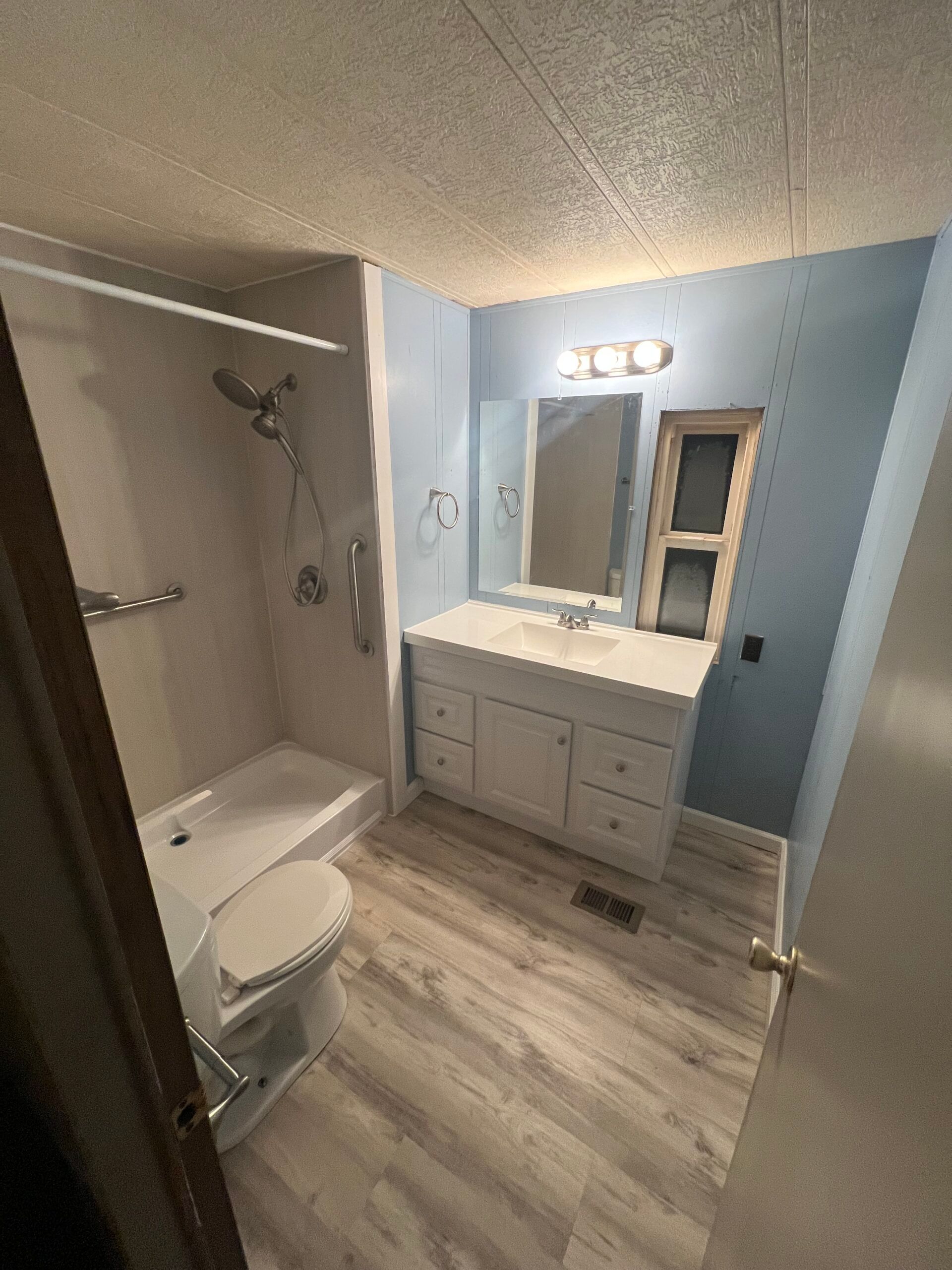 Small bathroom with tub-shower, toilet, vanity, and mirror in light blue and gray tones.