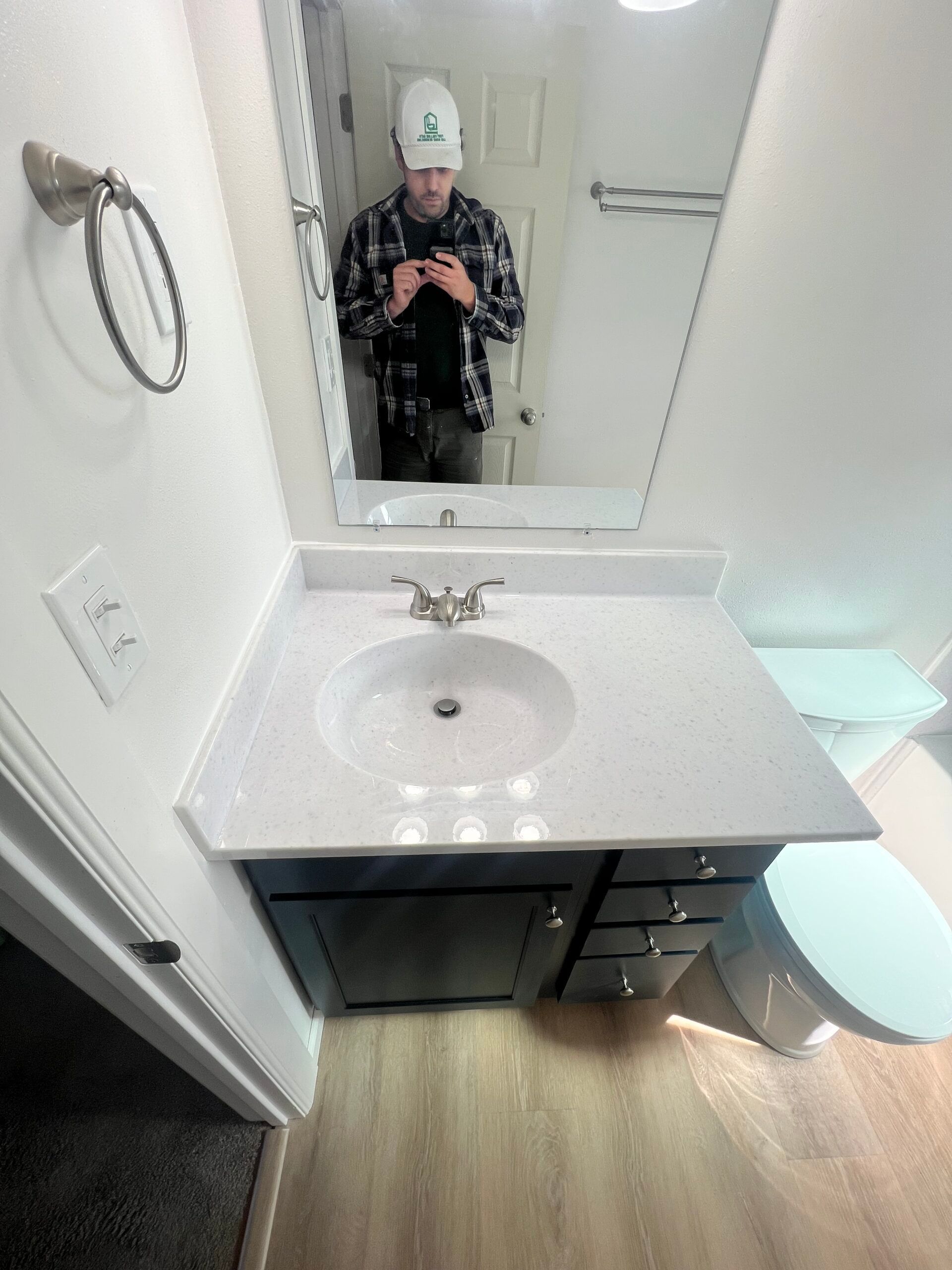 Bathroom vanity with sink, mirror, and a person taking a mirror selfie in a small white room.