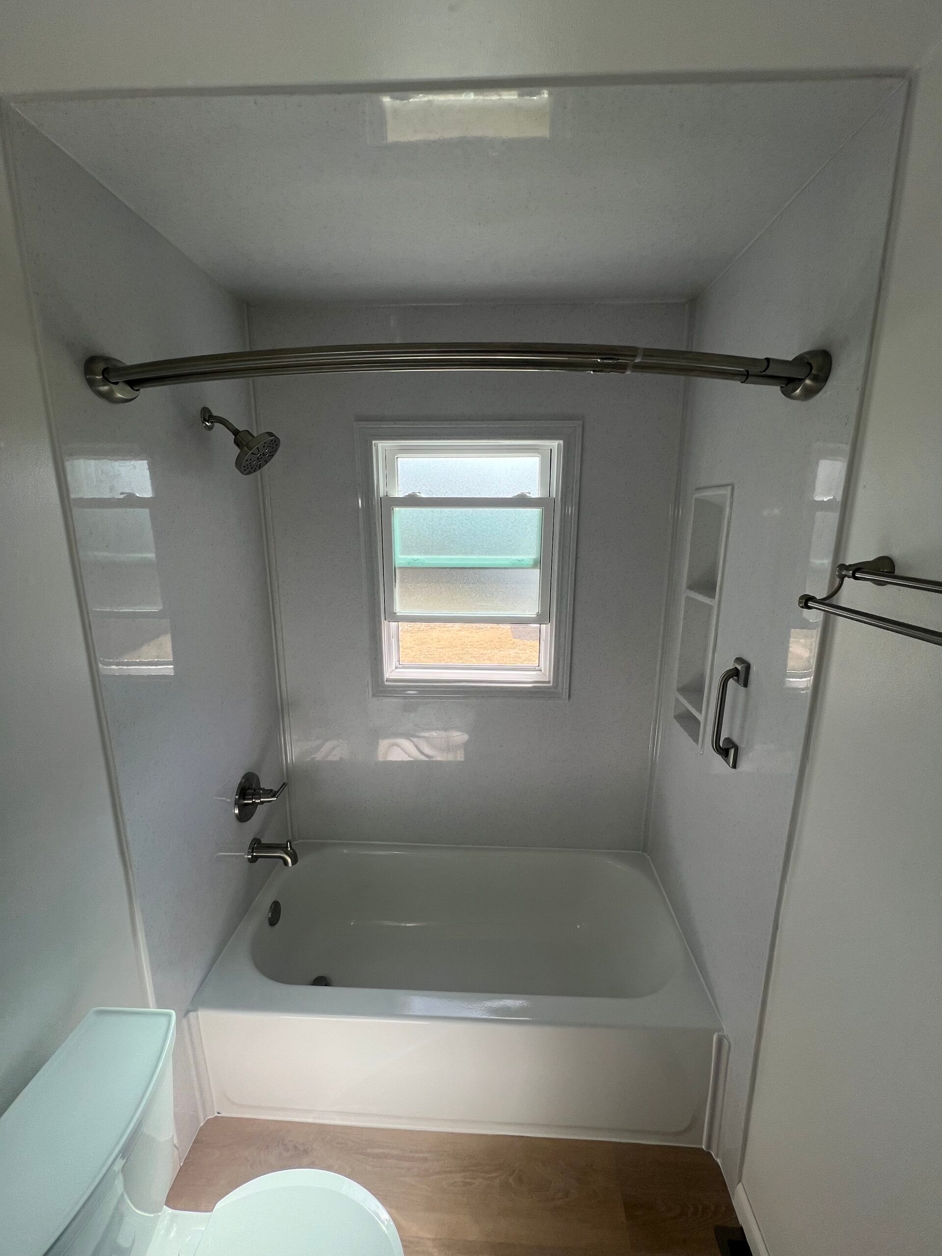 White bathroom with a bathtub-shower combo, small window, grab bars, and tiled walls.