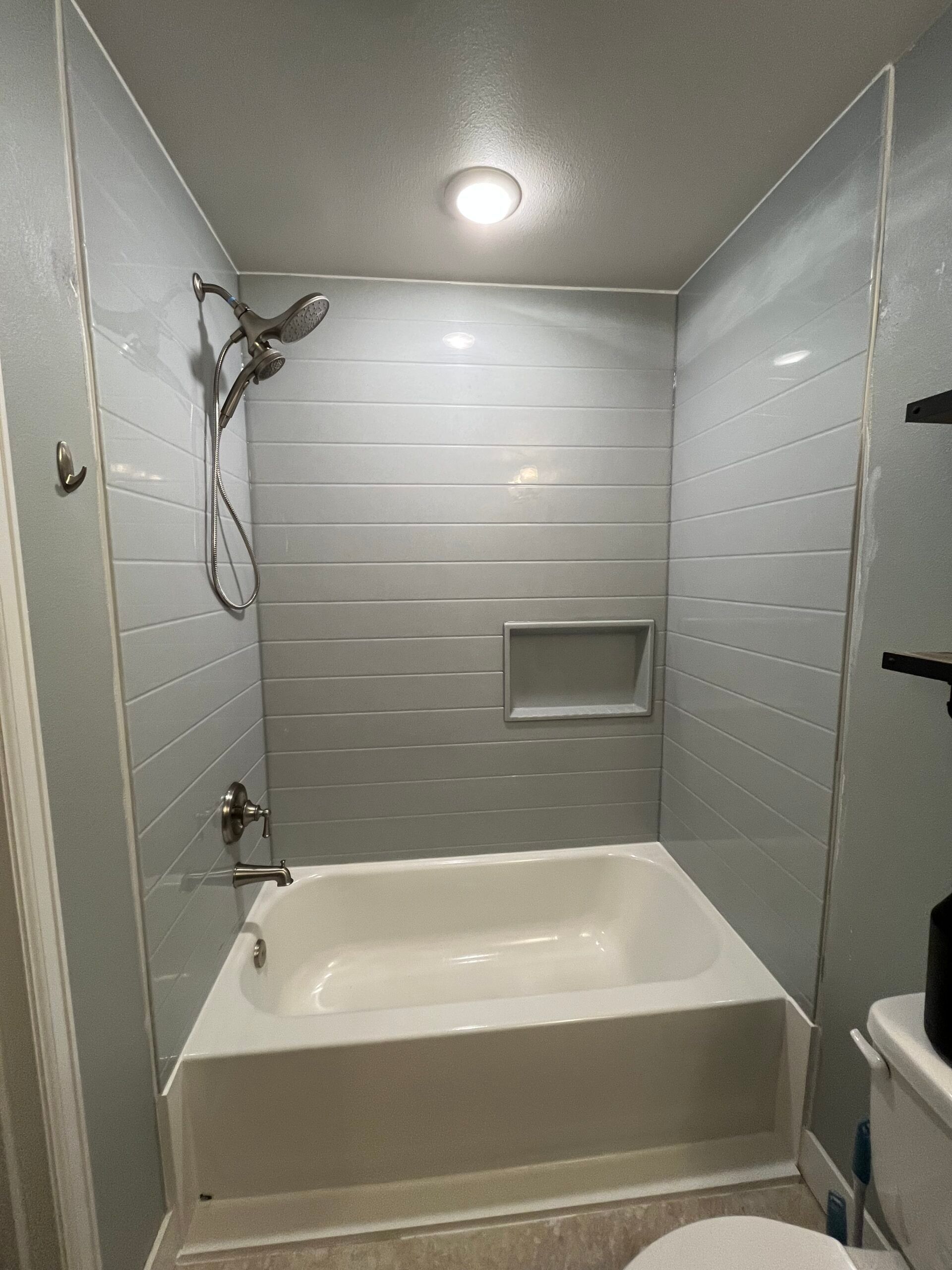 Compact tiled bathroom with a bathtub, showerhead, recessed shelf, and ceiling light