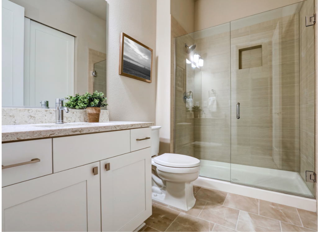 A bathroom with a toilet , sink and shower with a glass door.