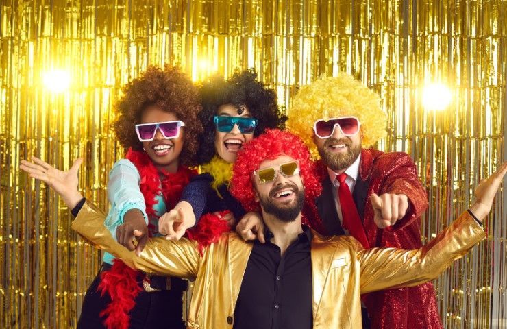 Four costumed performers in sunglasses pose in front of a gold tinsel backdrop