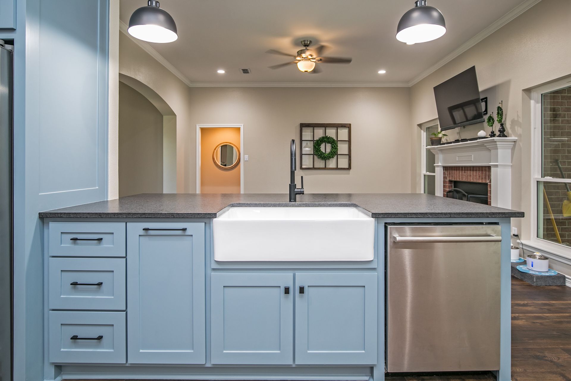 A kitchen with blue cabinets , a white farmhouse sink , and a stainless steel dishwasher.