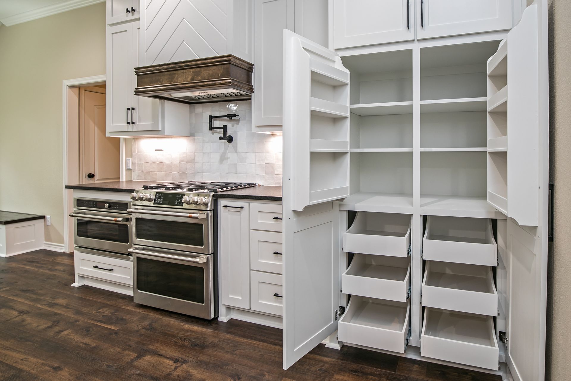 A kitchen with white cabinets , stainless steel appliances , and a pantry with drawers.