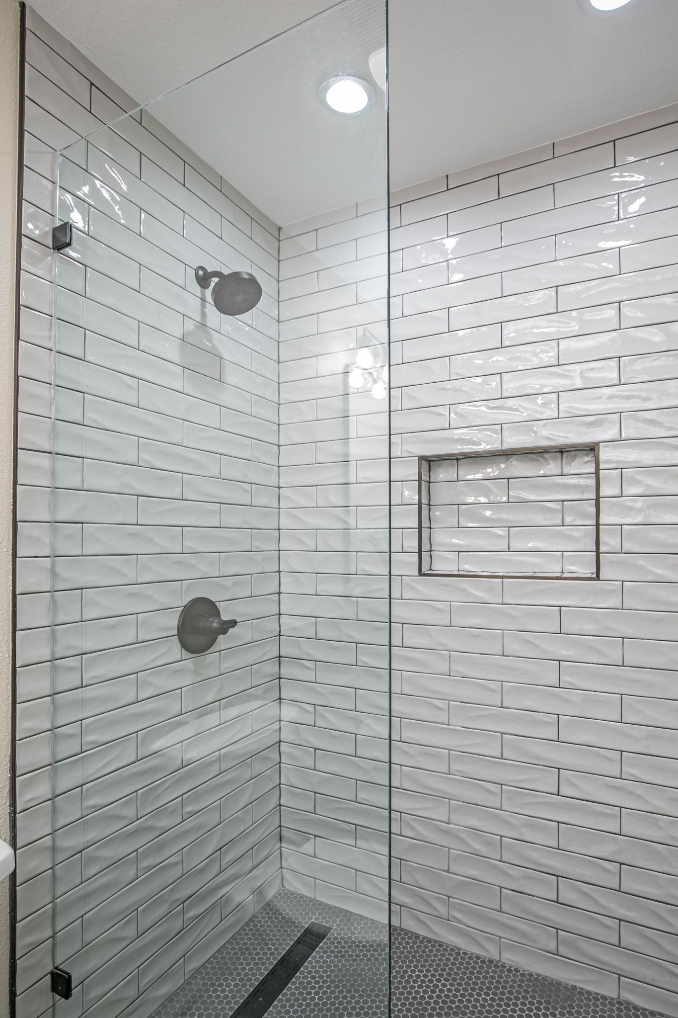 A walk in shower with white tiles and a glass door.