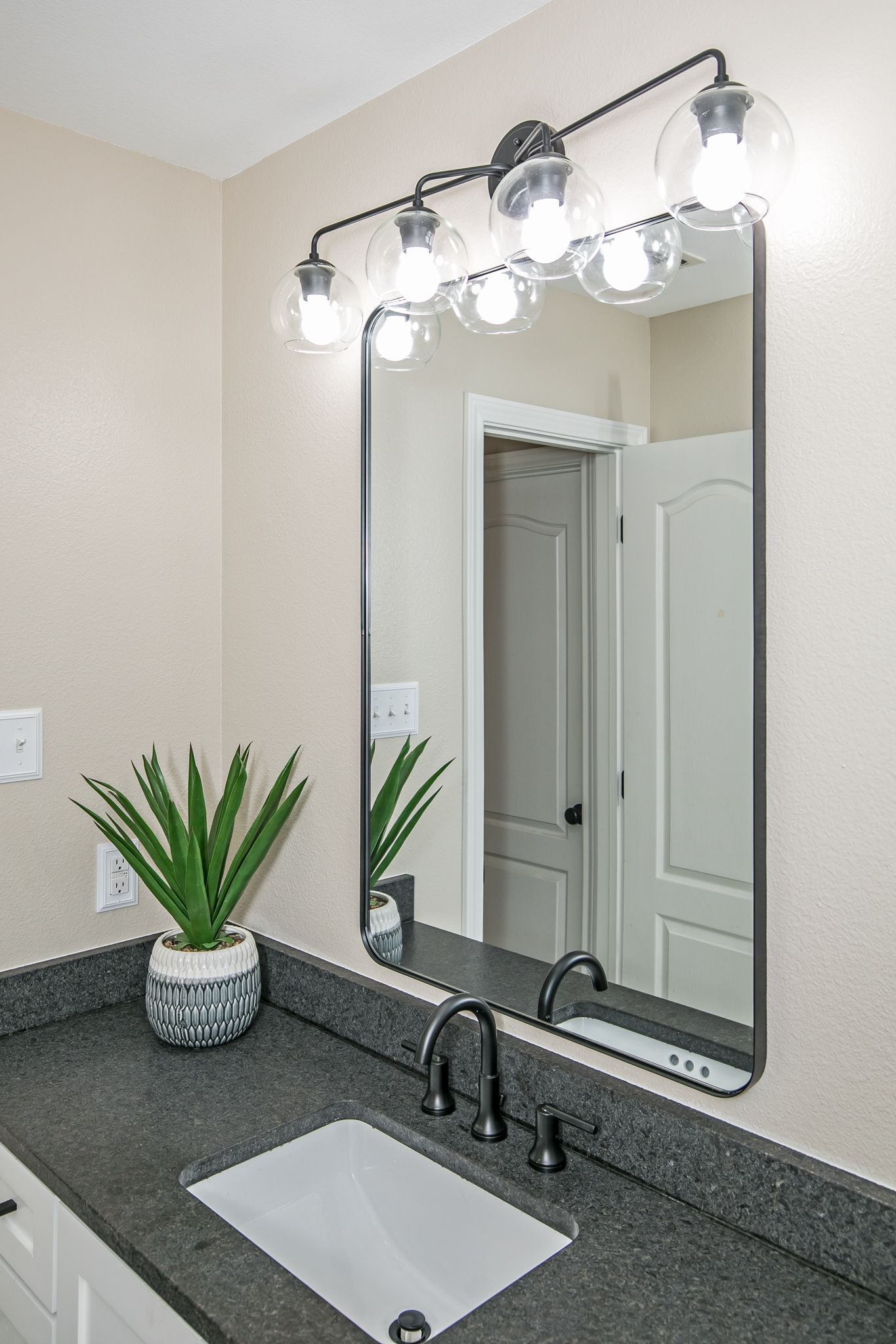 A bathroom with two mirrors , a sink and a potted plant.