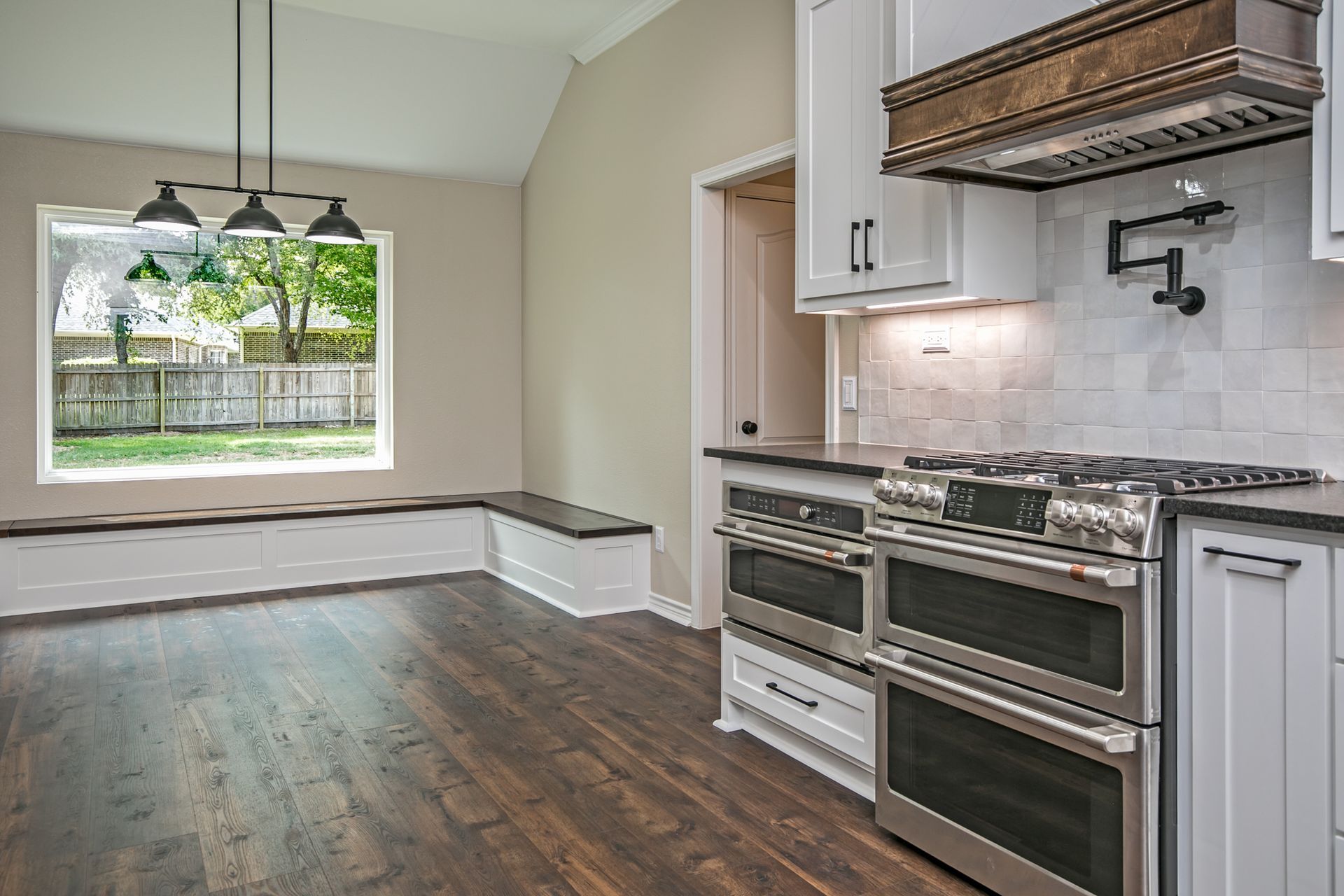 A kitchen with stainless steel appliances , white cabinets , hardwood floors and a large window.