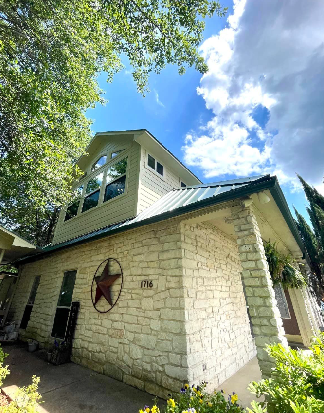 A white brick house with a green roof and a red star on the side.