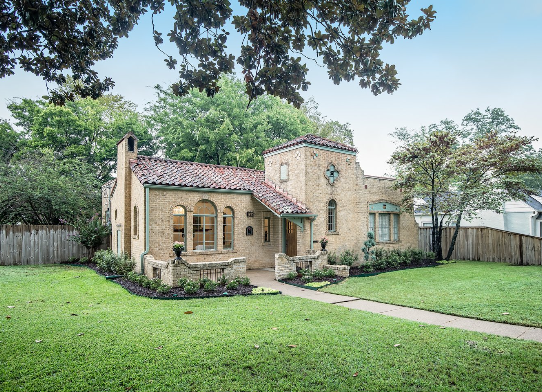 A large brick house with a red tile roof is surrounded by trees and grass.