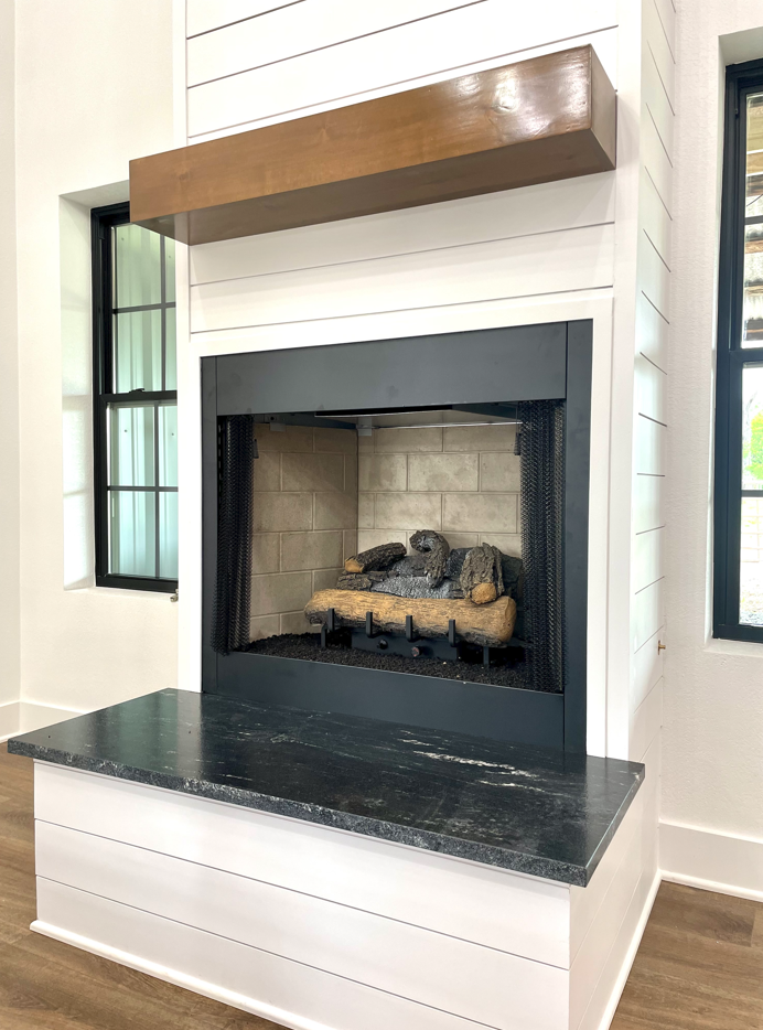 A fireplace with a wooden mantle and a black counter top in a living room.