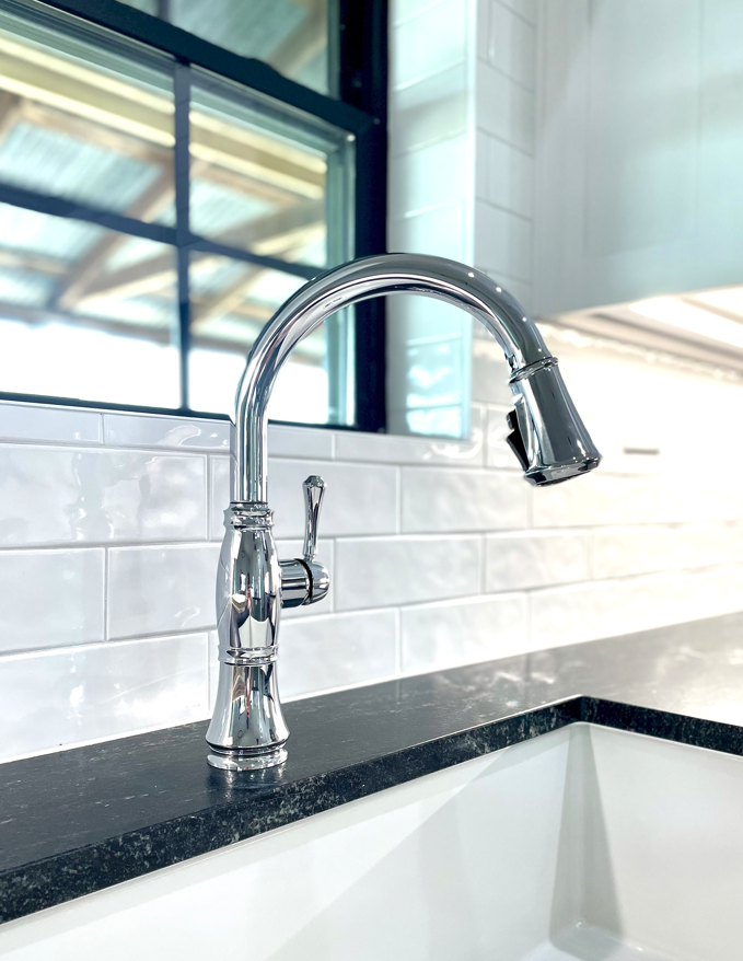 A kitchen sink with a chrome faucet and a black counter top.
