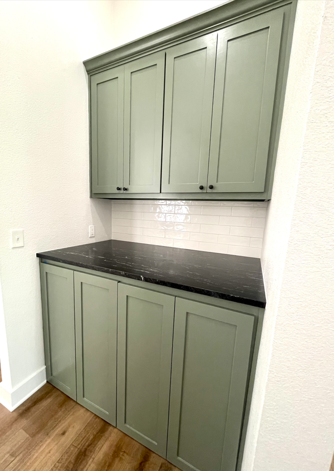 A kitchen with green cabinets and a black counter top.