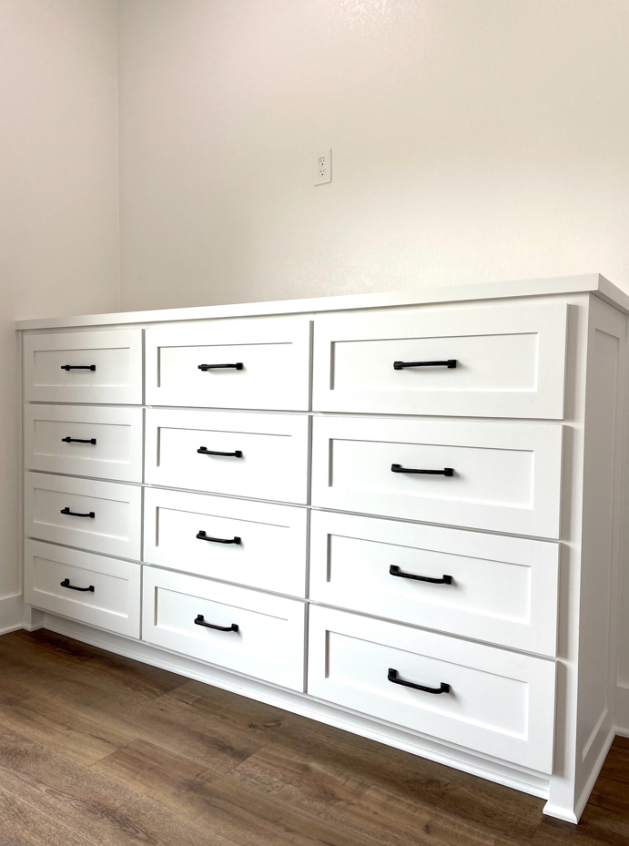 A large white dresser with black drawers in a room.