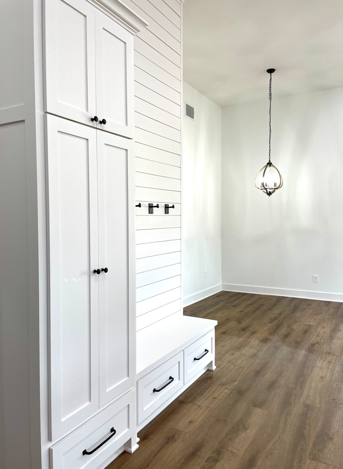 There is a bench in the middle of the room with white cabinets.