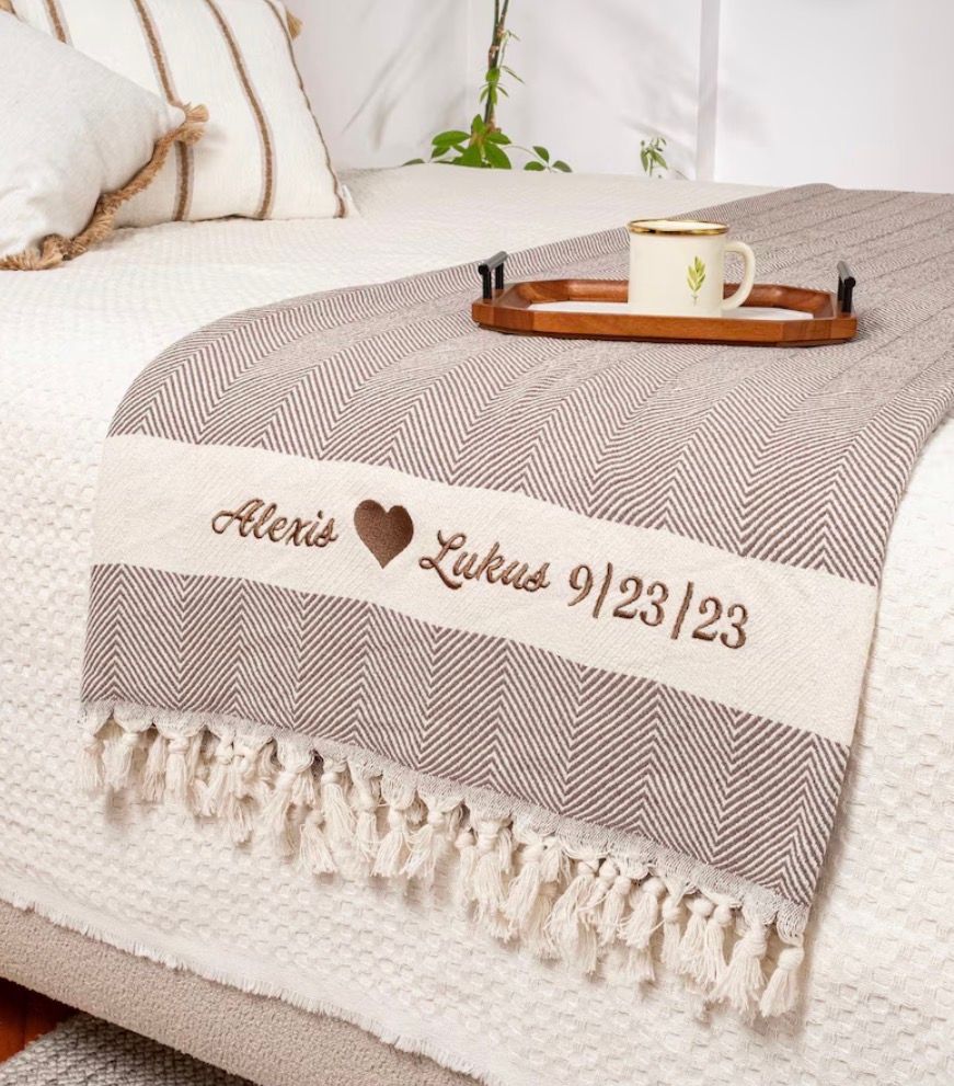 Personalized blanket with embroidered names, heart, and wedding date on a bed with a tray and mug.