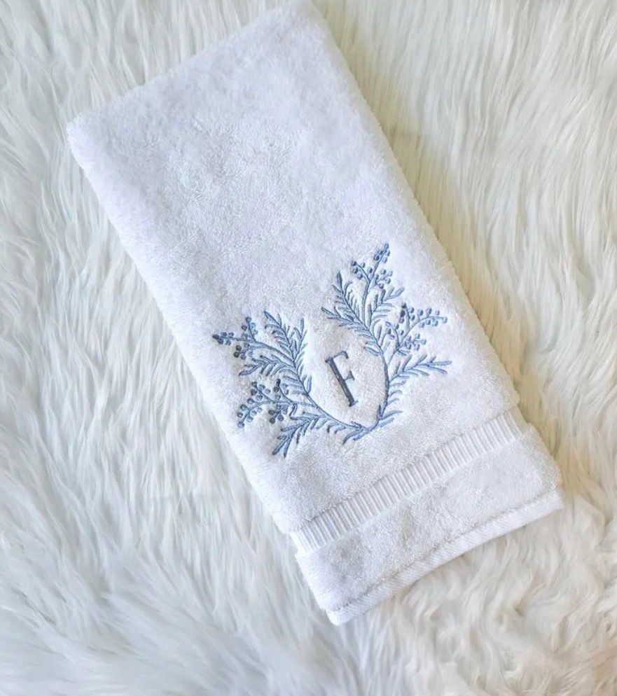 White hand towel with embroidered blue floral design and the letter 