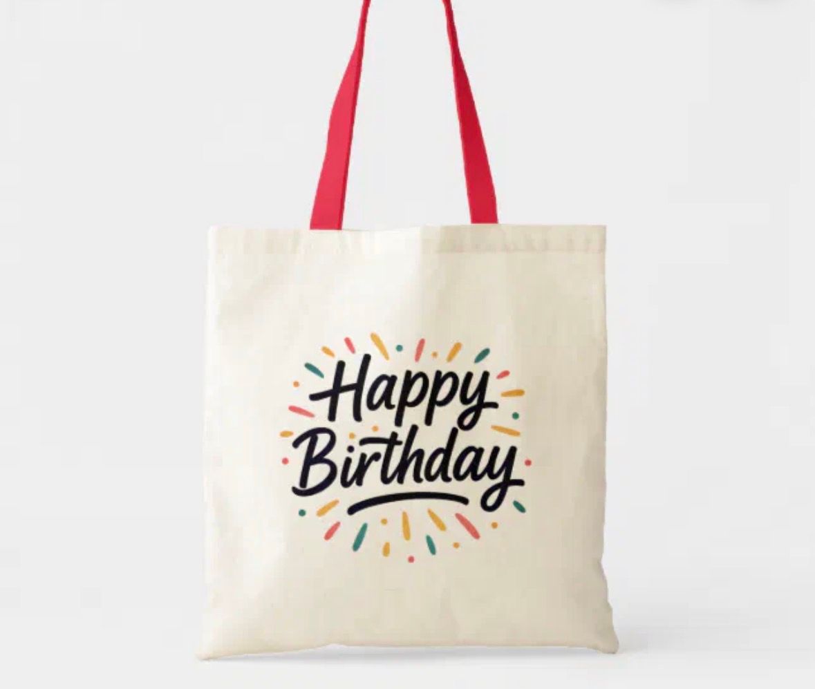Cream tote bag with red handles, “Happy Birthday” in black script, colorful burst design.
