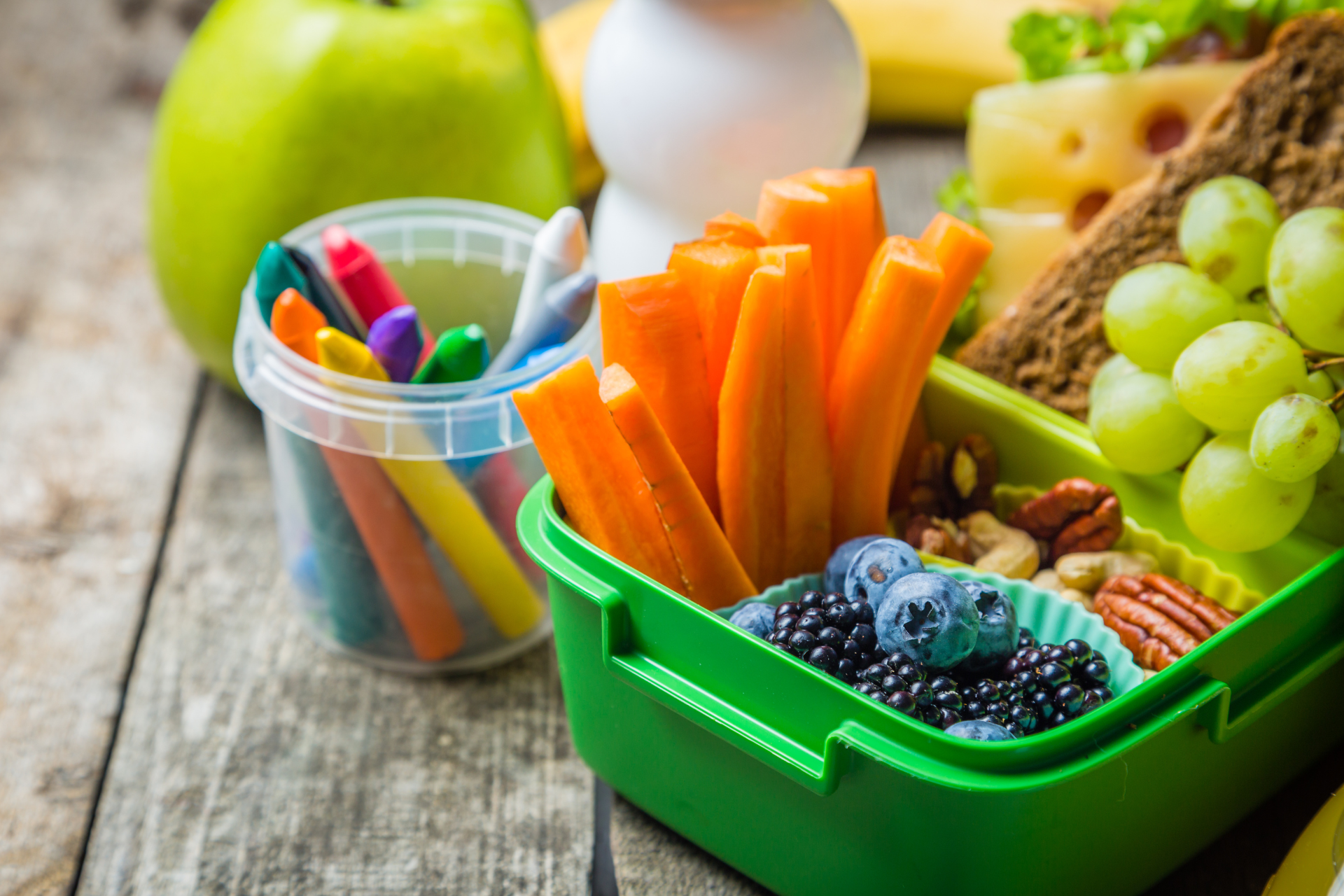 A green lunch box filled with fruits and vegetables on a wooden table.