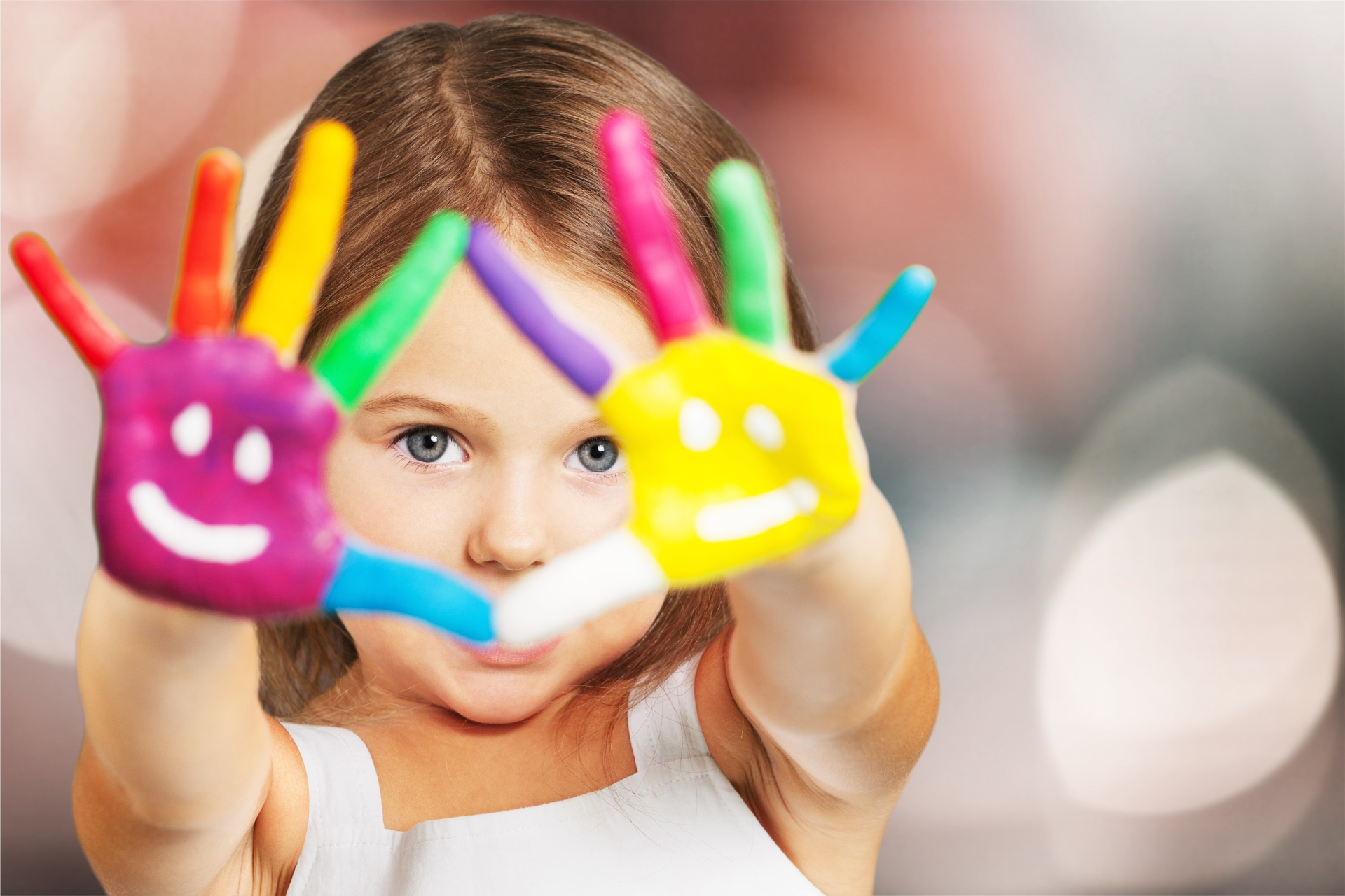 A little girl is holding her hands painted with smiley faces.