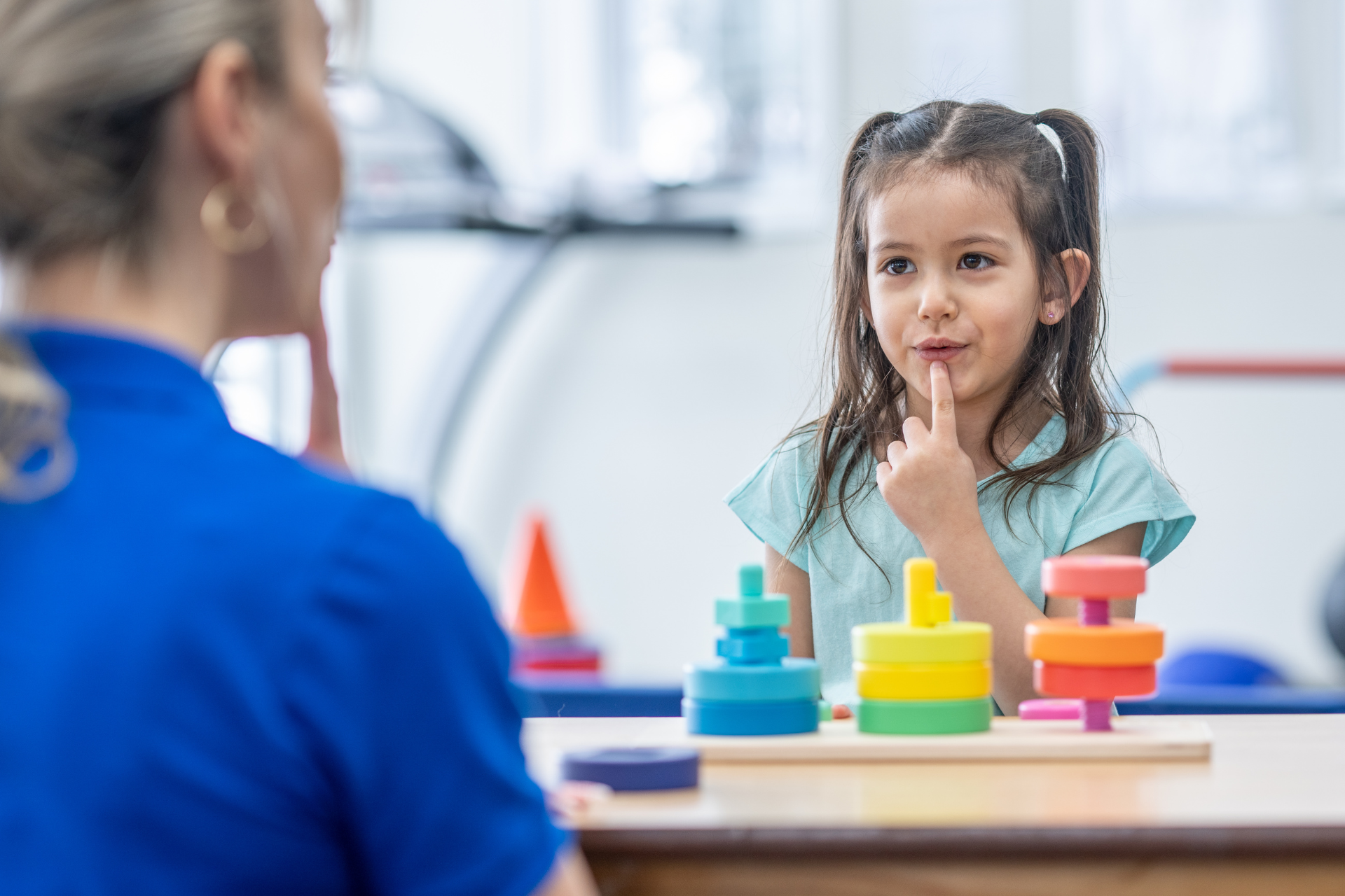 A little girl is sitting at a table with a stack of blocks.