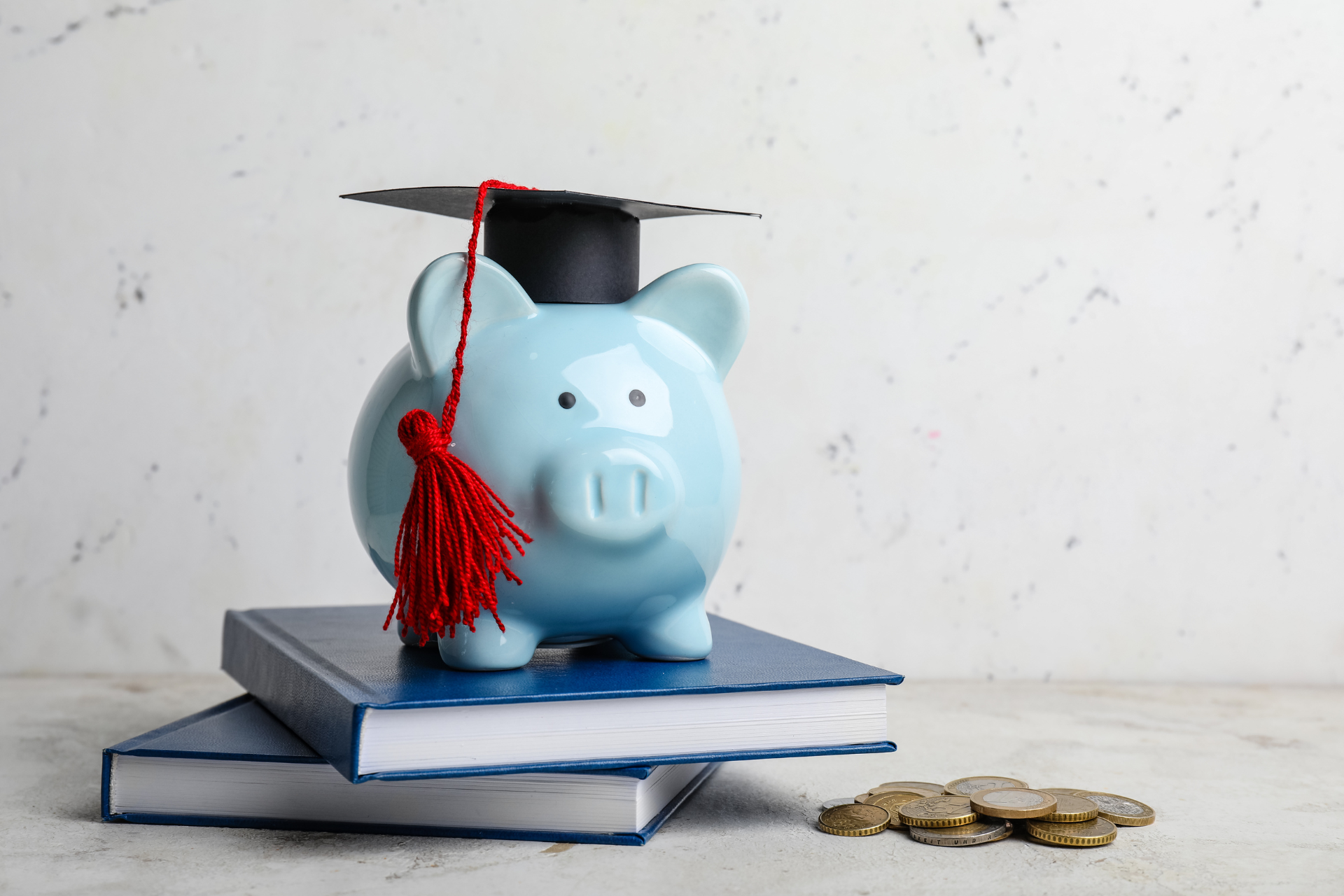 A piggy bank wearing a graduation cap is sitting on top of a stack of books.