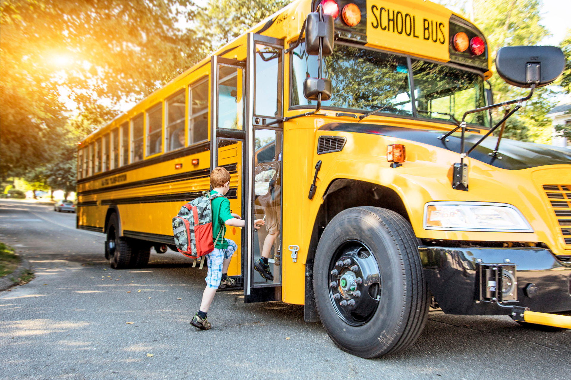 A young boy is getting off a yellow school bus.