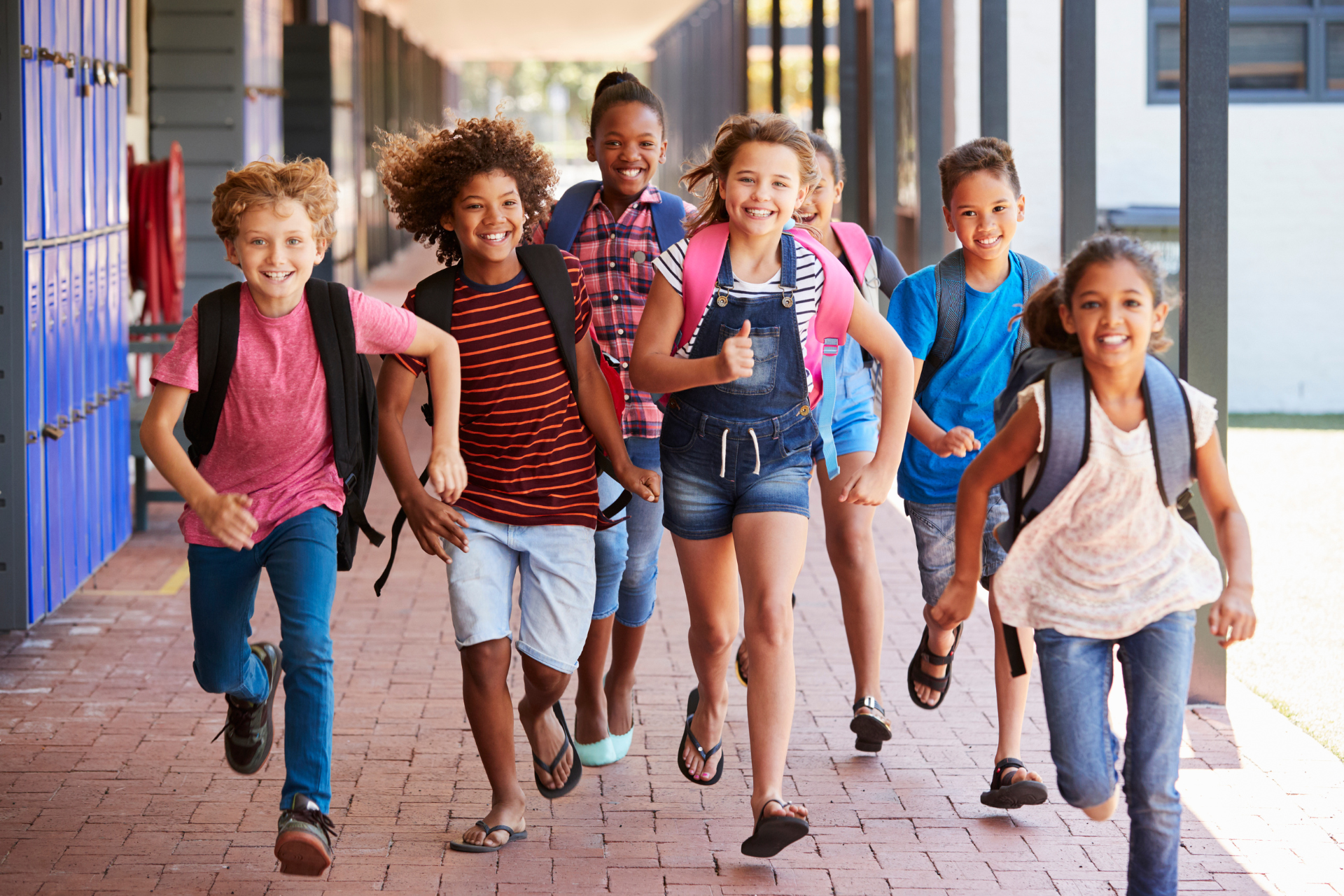 A group of children with backpacks are running down a hallway.