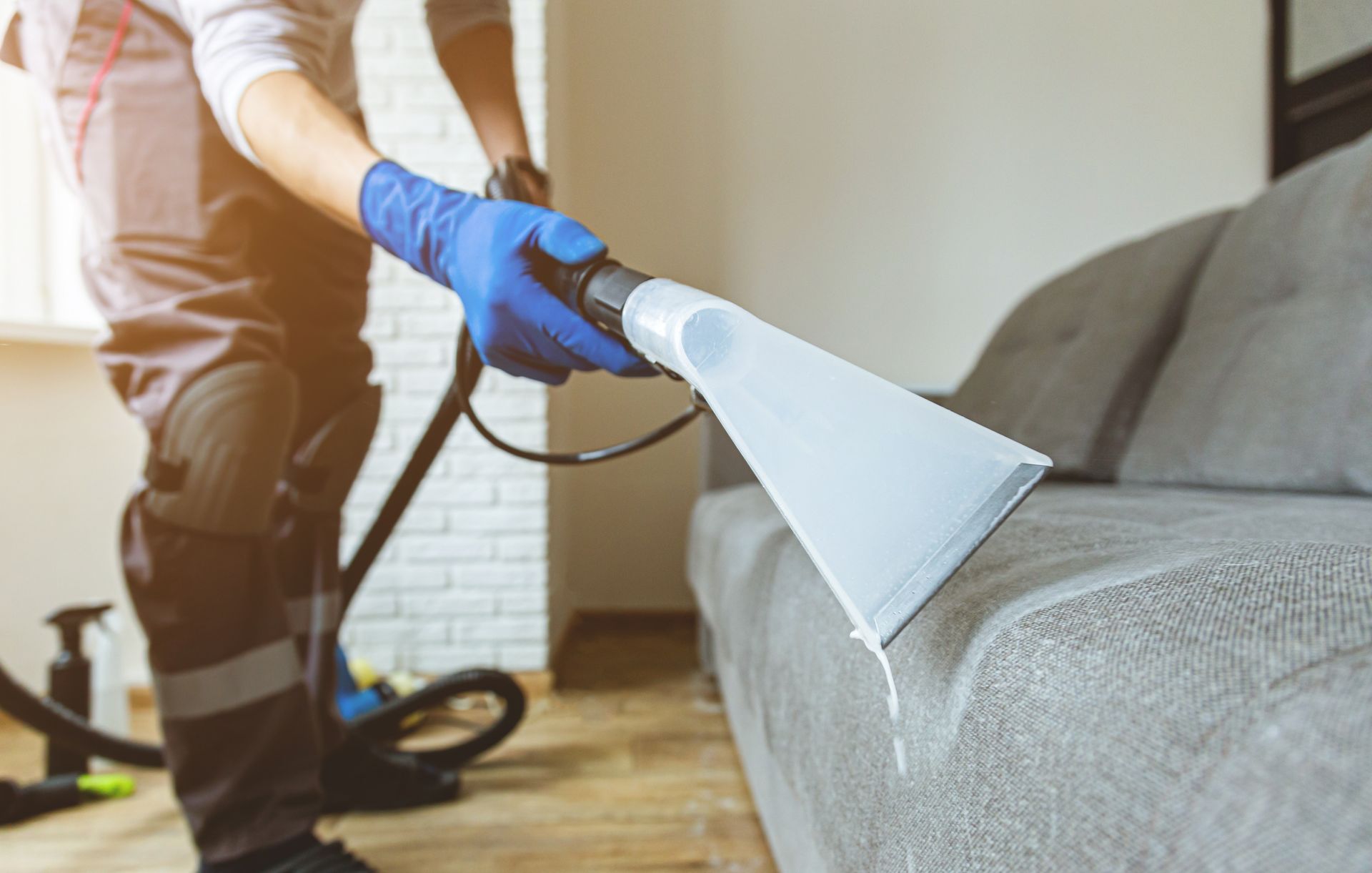 A man is cleaning a couch with a vacuum cleaner.