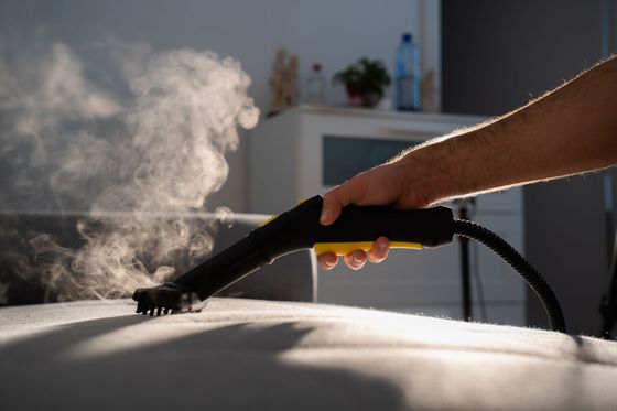 A person is using a steam cleaner to clean a couch.