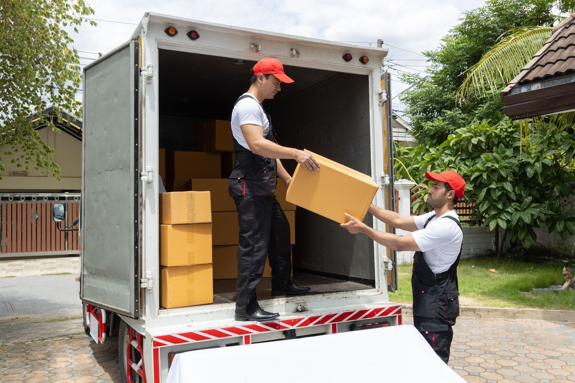 Two workers load cardboard boxes into white delivery truck.