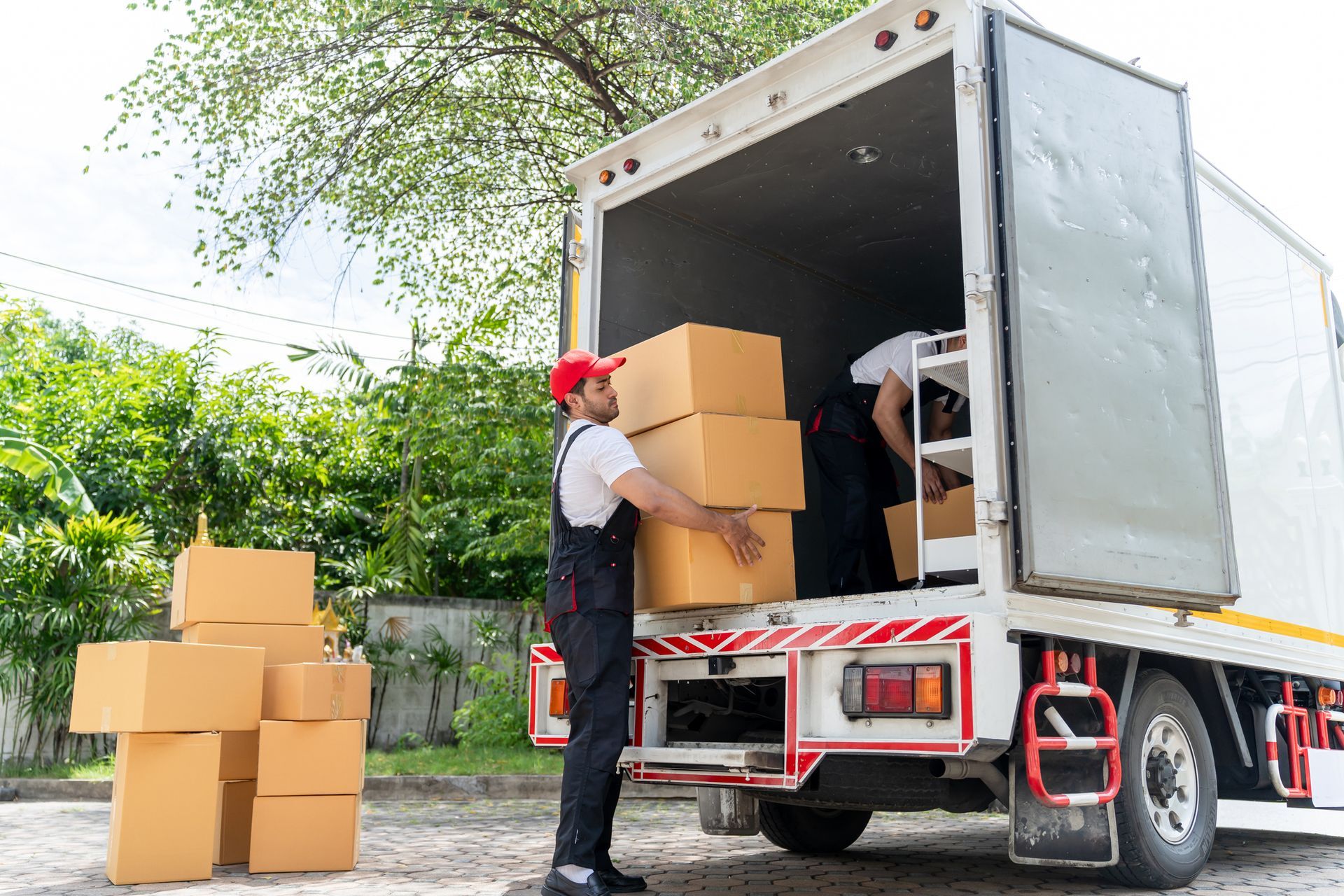 Workers load cardboard boxes into truck on sunny afternoon.