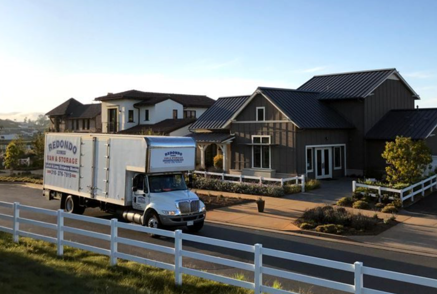 Moving truck in front of a modern gray house, white fence, bright sunny day. Moving truck in front of a modern gray house, white fence, bright sunny day.