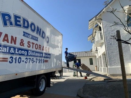 A Redondo Van & Storage truck parked next to a loading dock with two movers transporting items.