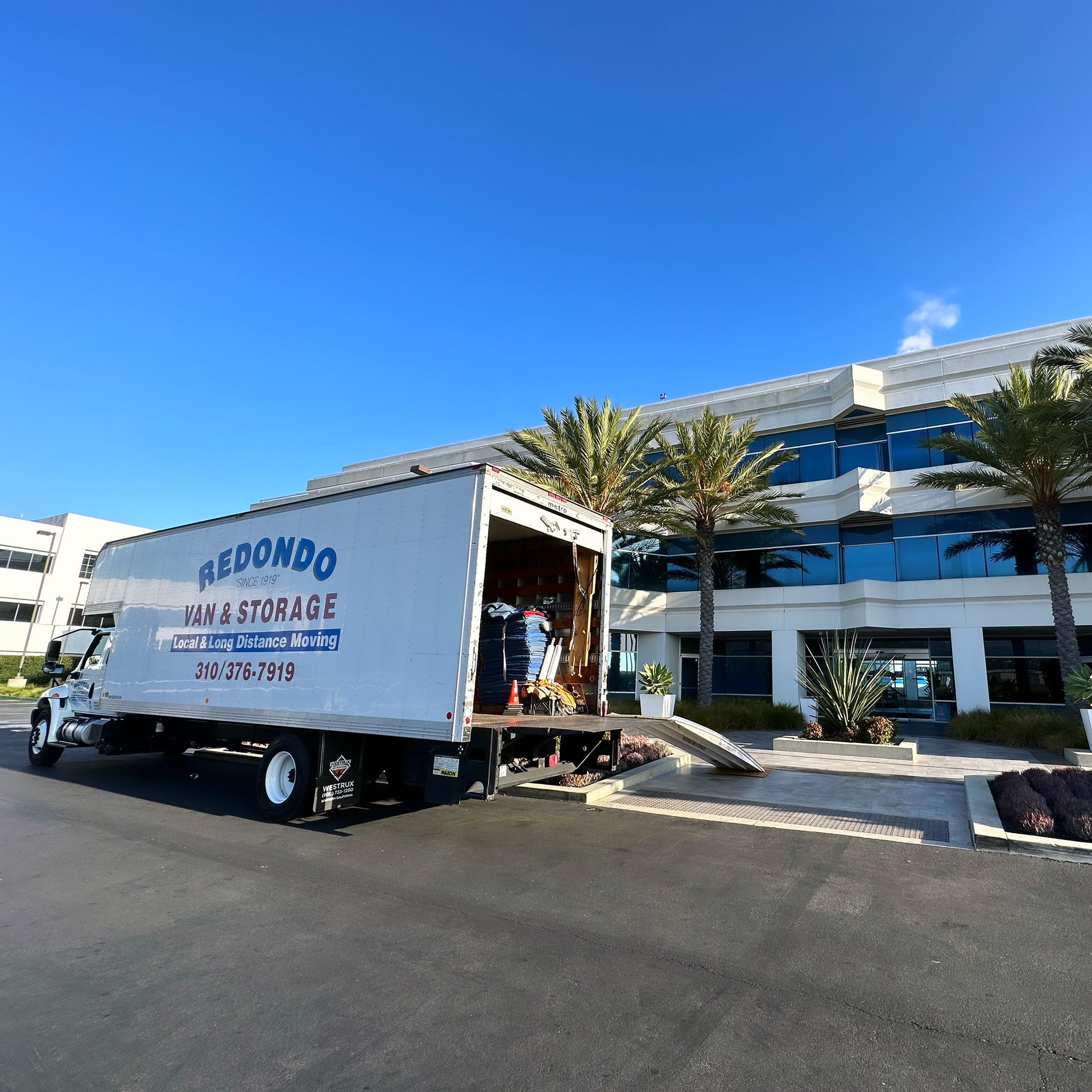 A moving truck is parked outside the building with a crew loading furniture. A moving truck is parked outside the building with a crew loading furniture.