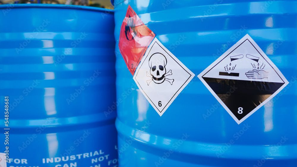 Two blue barrels with hazard warning labels: one with a skull, the other with a hand pouring liquid, symbol 8.