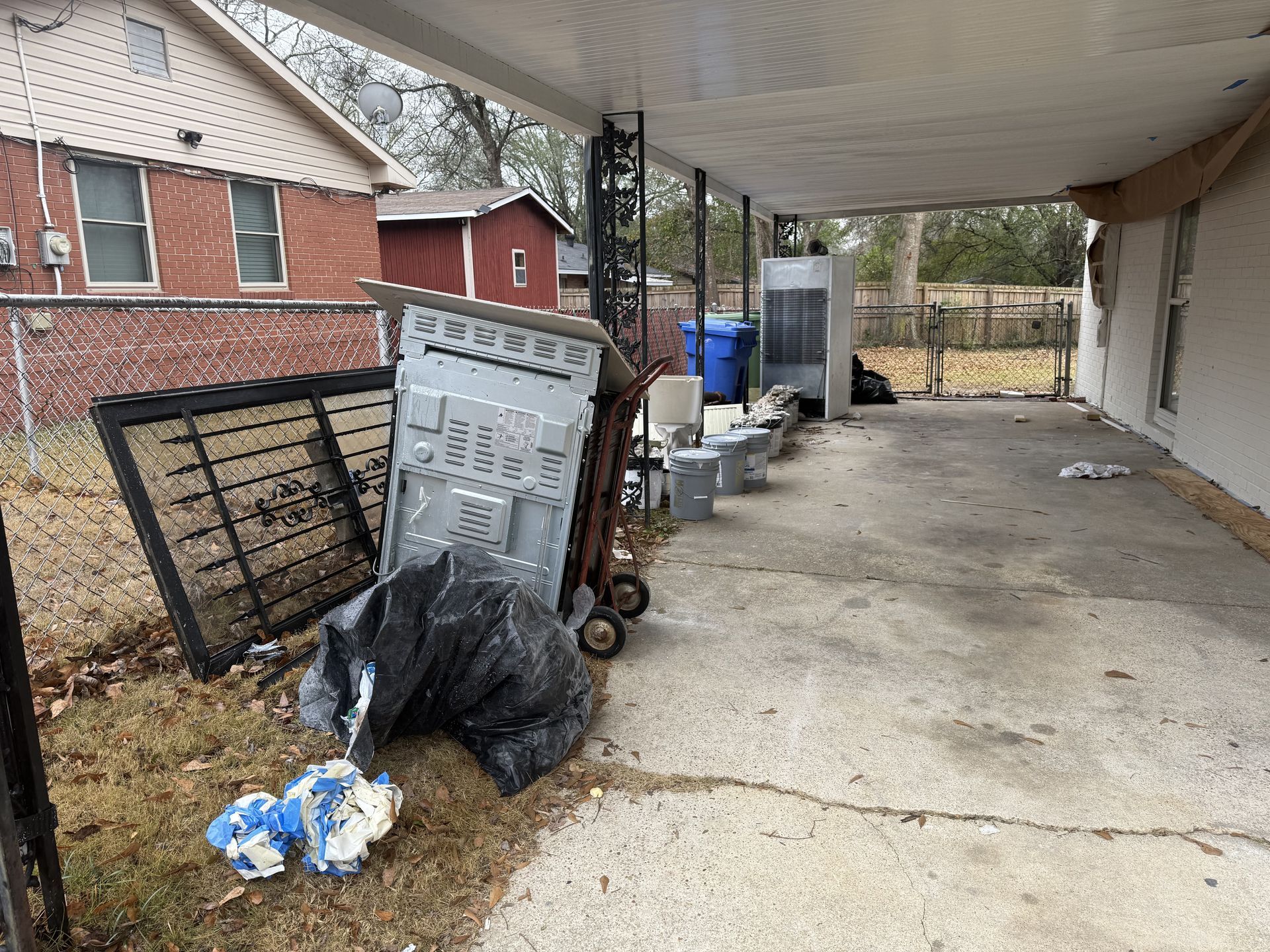 A cluttered patio with trash, an appliance, and a brick house in the background.