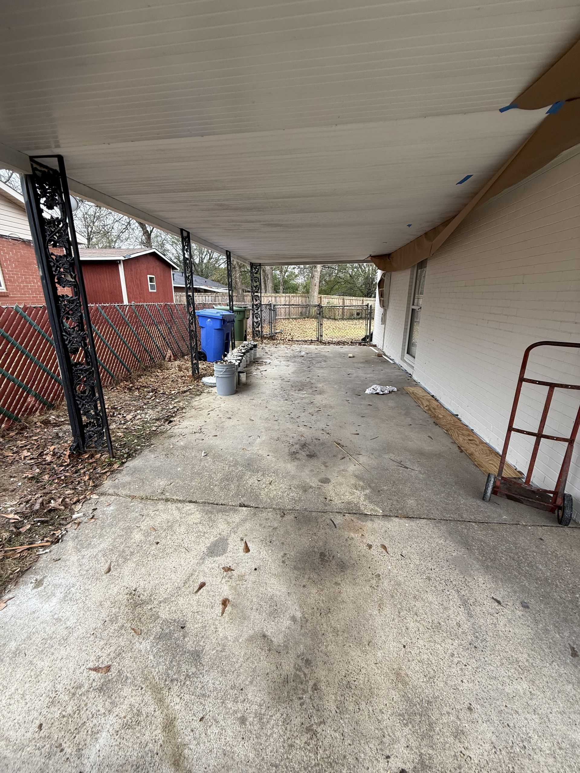 Covered concrete patio with black supports, extending from a white house.