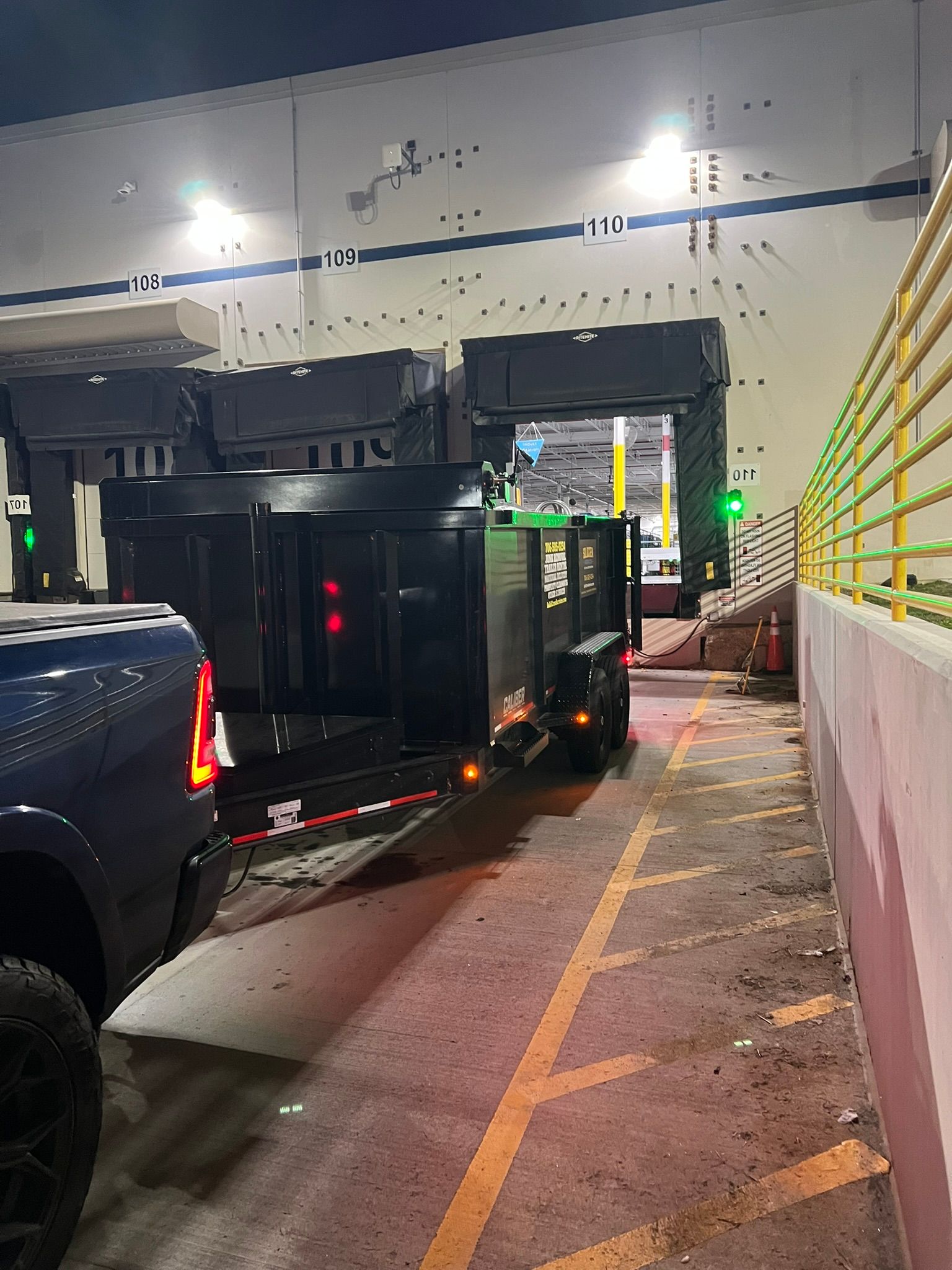 A pickup truck towing a black trailer at a loading dock at night.