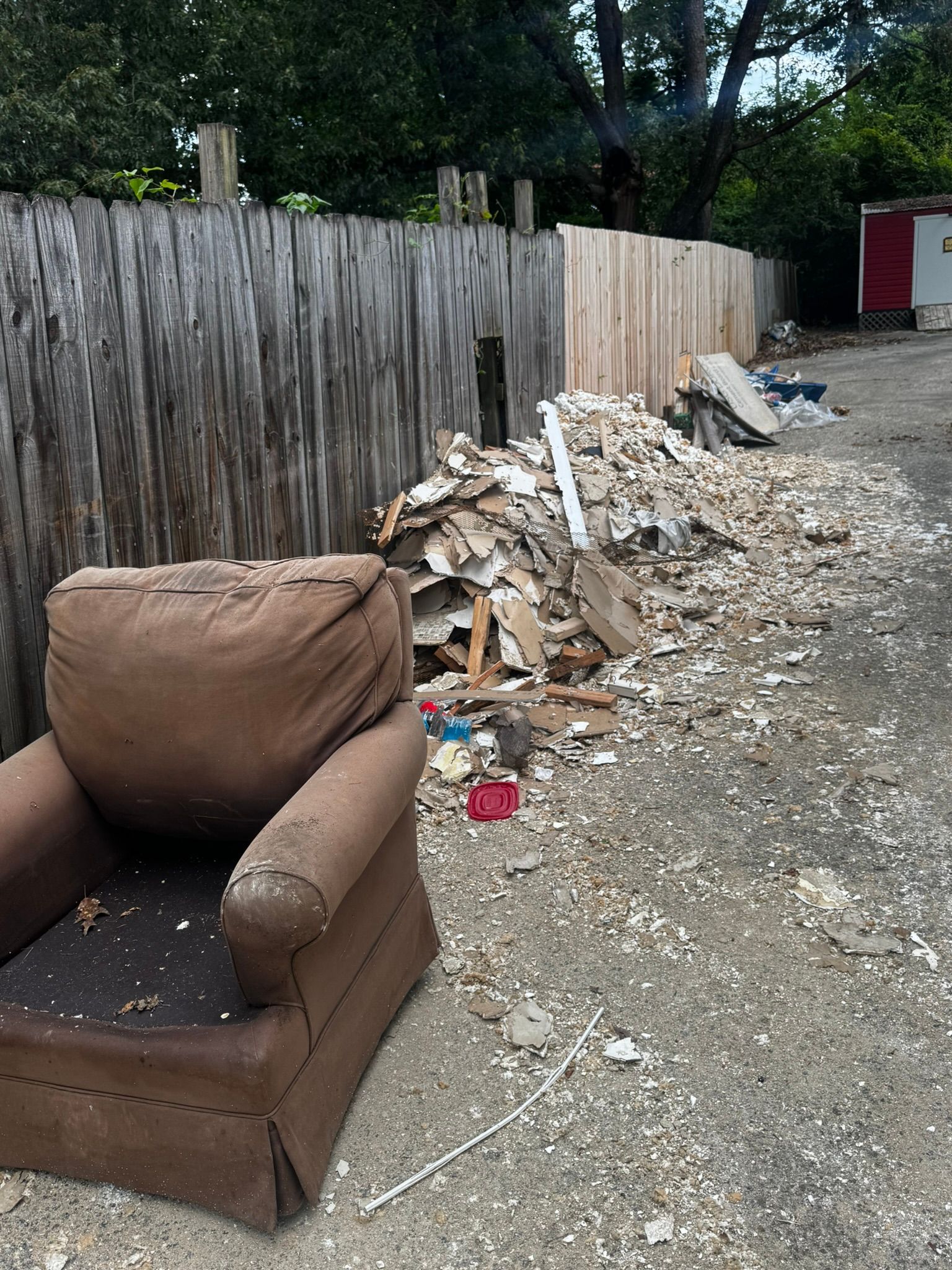 Old brown armchair and debris piled next to a wooden fence.