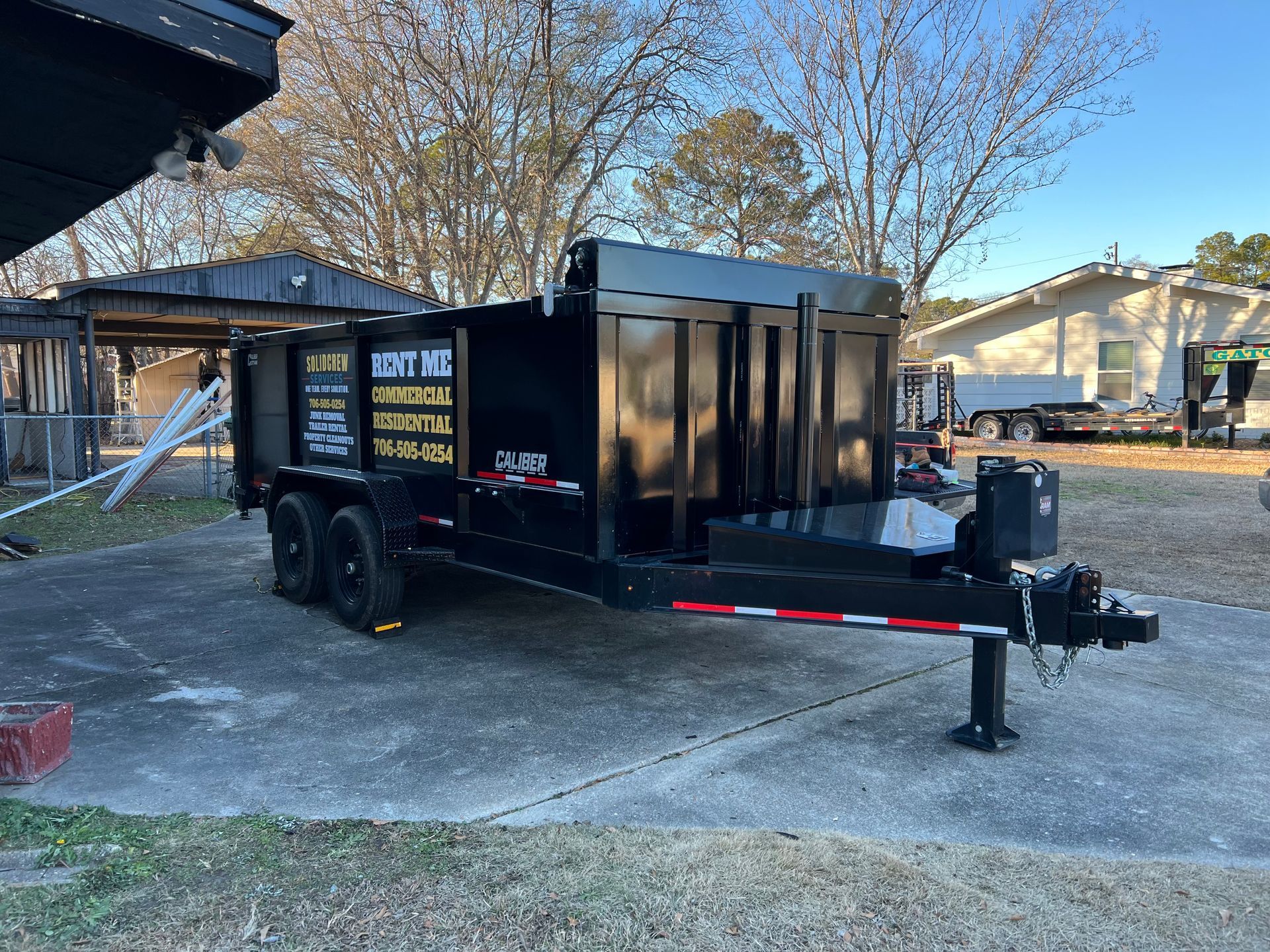 Black dump trailer parked outdoors on a sunny day.