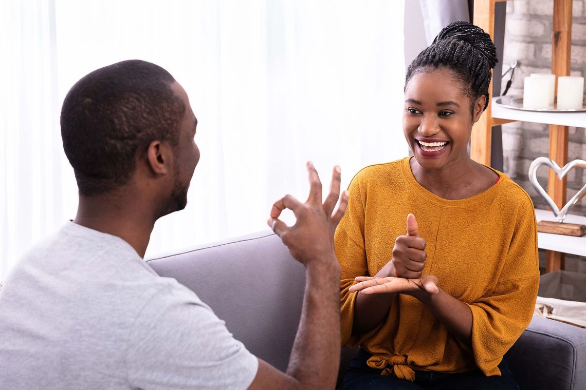 A man and a woman are sitting on a couch talking in sign language.