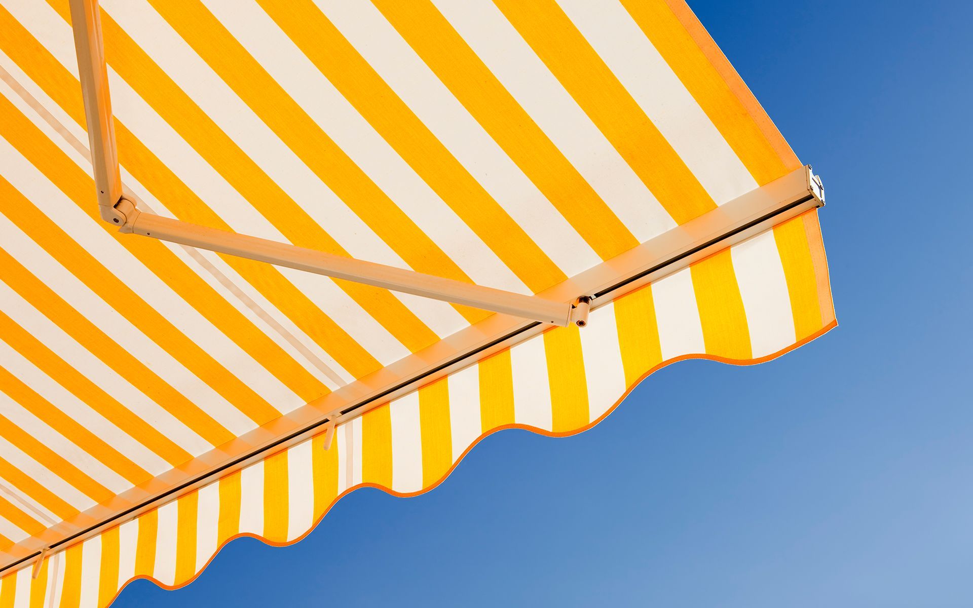 A yellow and white striped awning is against a blue sky.