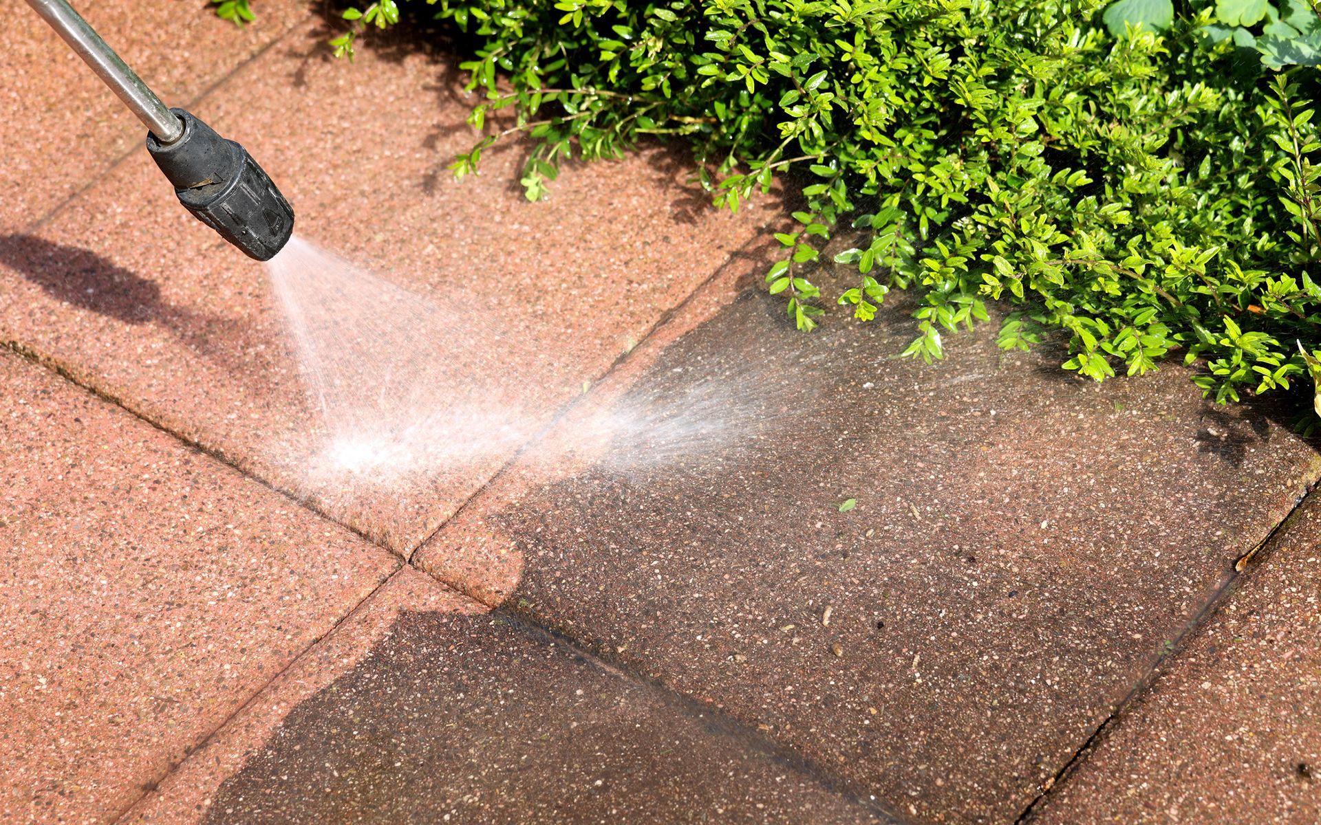 A person is using a high pressure washer to clean a brick walkway.