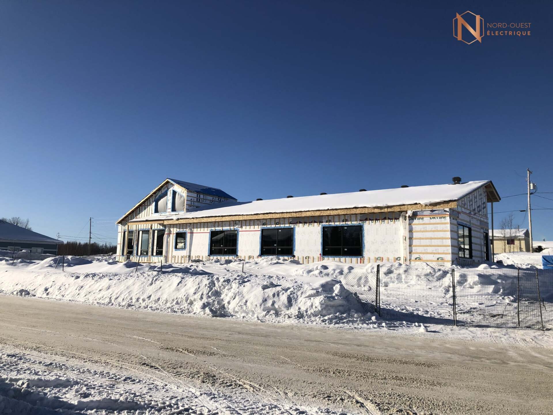 Une maison est en construction dans la neige à côté d'une route.