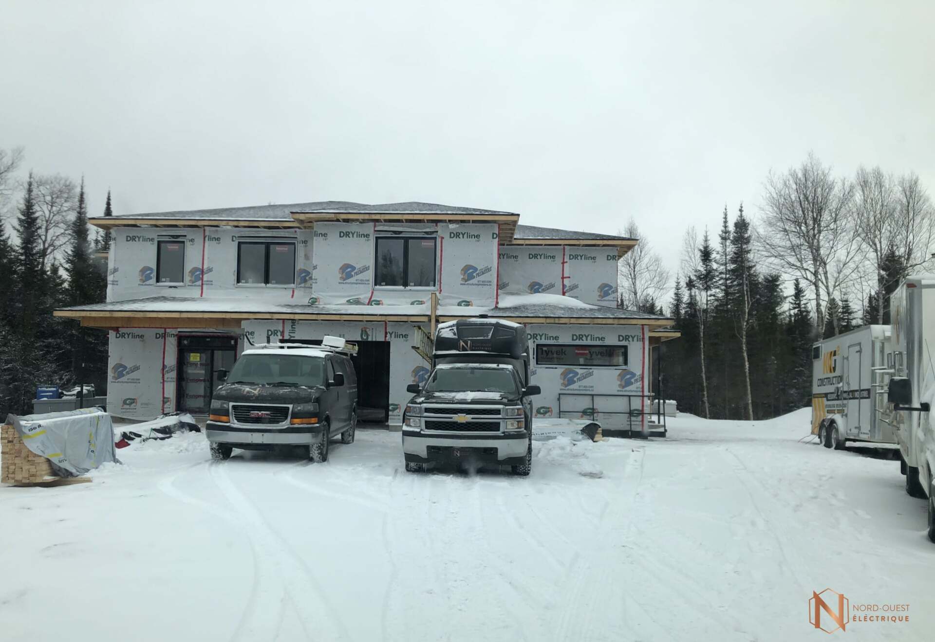 Deux camionnettes sont garées devant une maison en construction sous la neige.