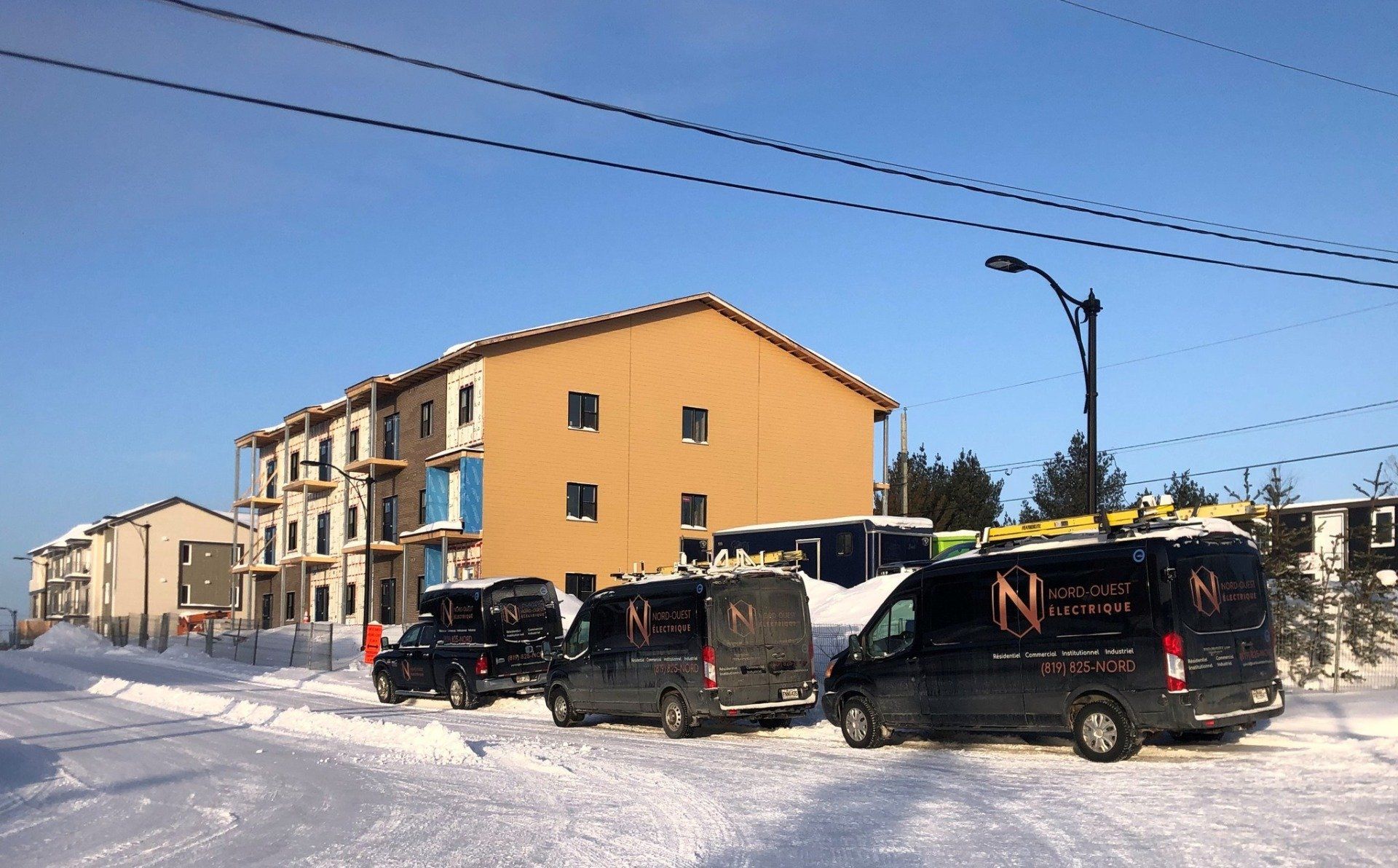 Une rangée de camionnettes est garée dans la neige devant un bâtiment en construction.