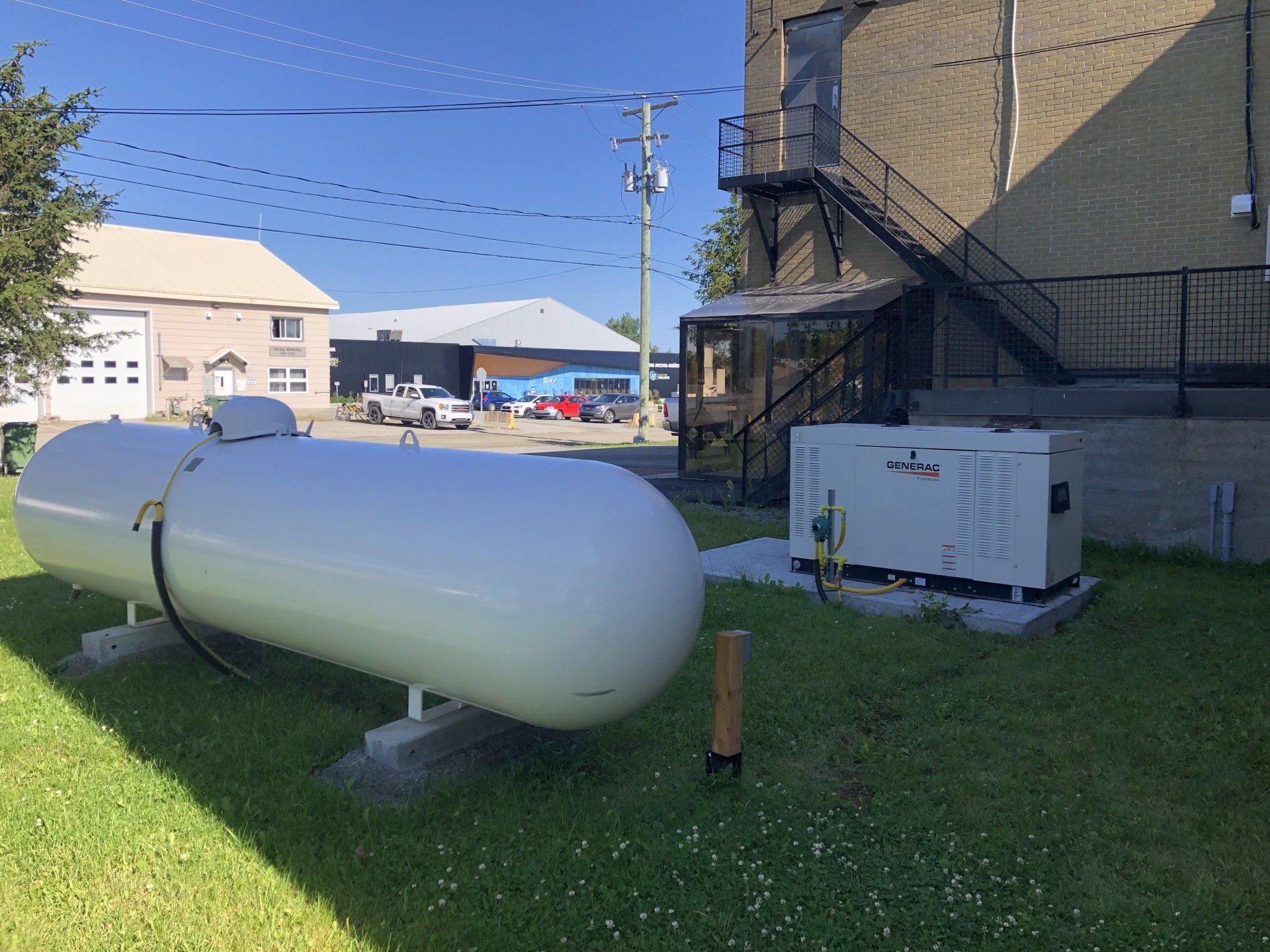 Un grand réservoir de propane blanc est posé dans l'herbe devant un bâtiment.