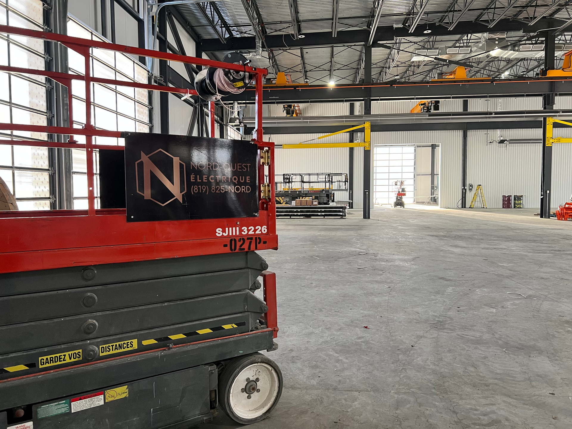 Un élévateur à ciseaux rouge est garé dans un grand entrepôt vide.